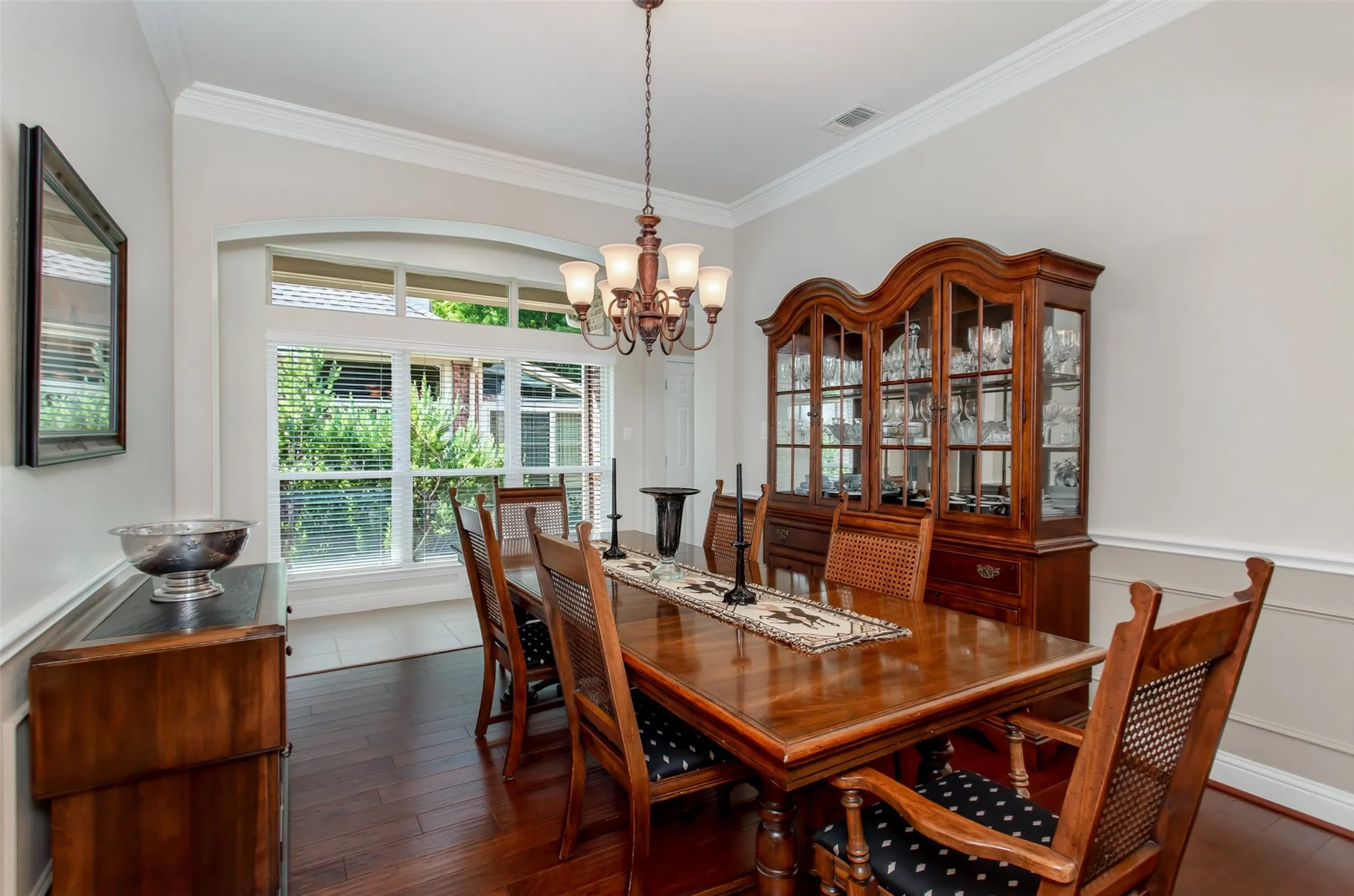 Formal dining space featuring crown molding, wood-finish flooring, an arched window, and wainscoting