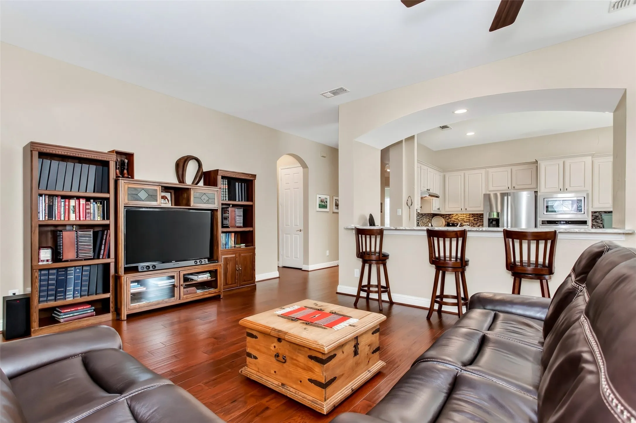 Hardwood flooring throughout, arched doorway, kitchen pass-through with breakfast bar, recessed lighting, and ceiling fan