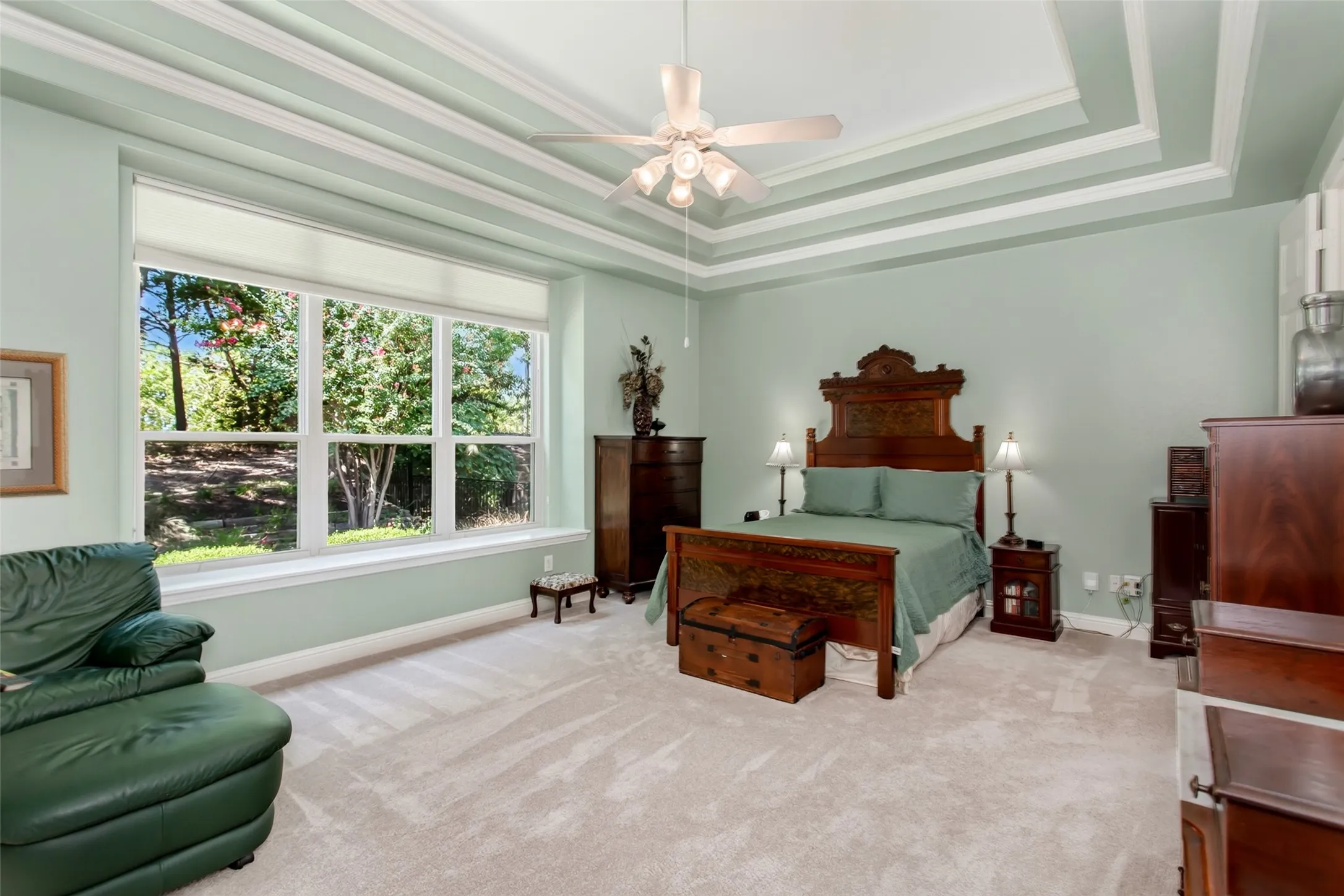 Tray ceiling with crown molding, ceiling fan, large window with sills, and carpeting