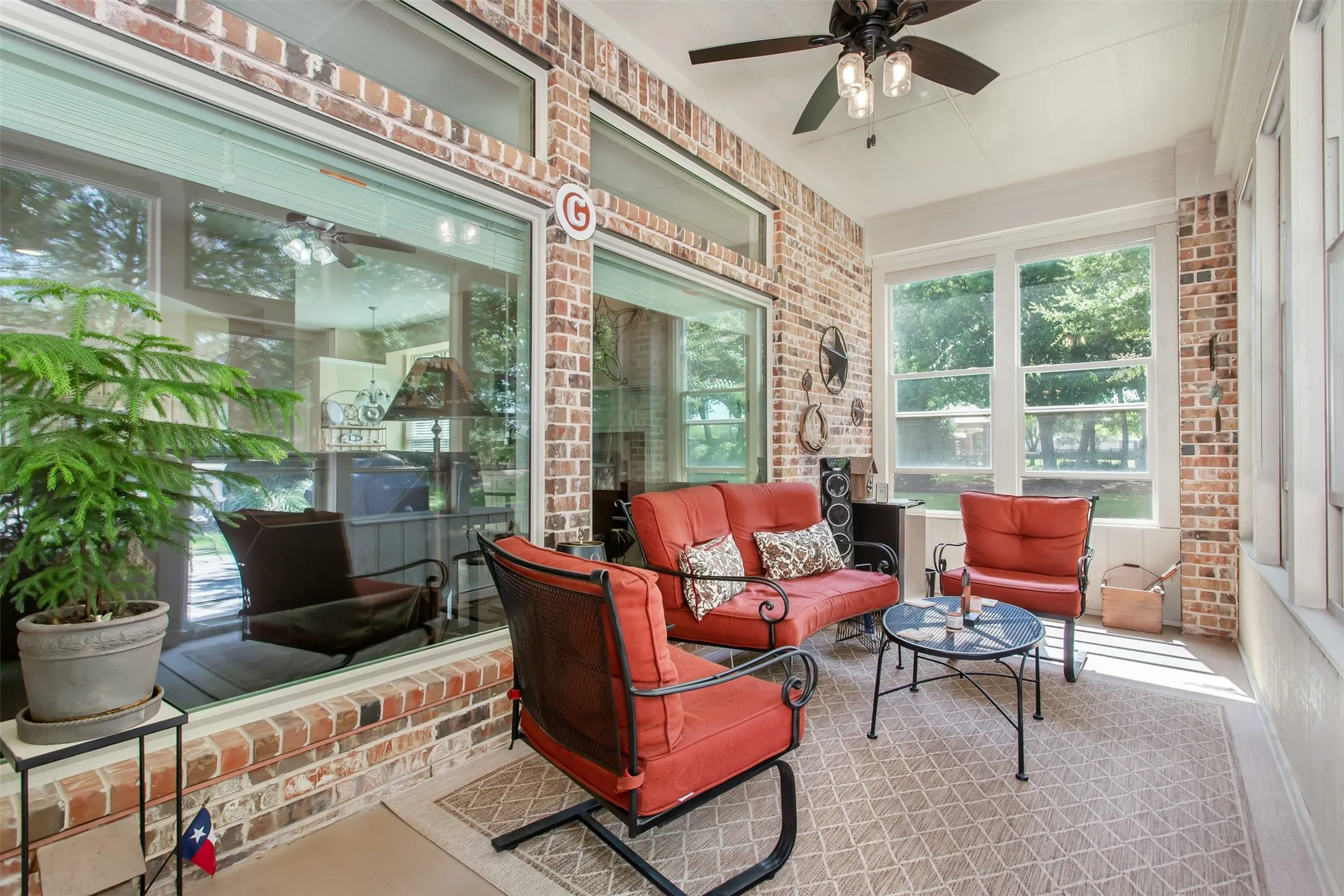 Brick-accented sunroom with large windows, transom windows, a ceiling fan with light fixture, and a screened enclosure