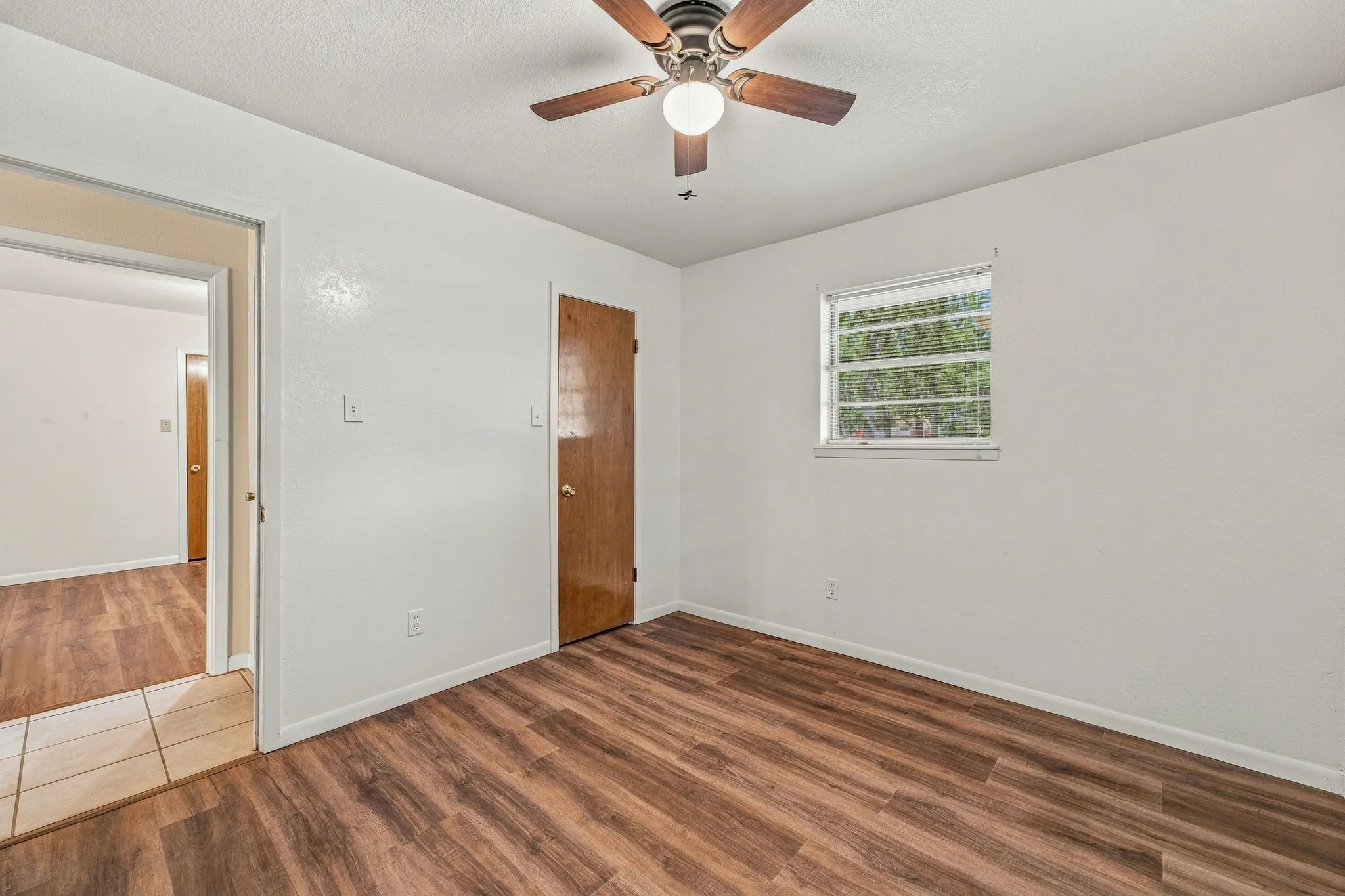 Wood-finish flooring, ceiling fan with integrated lighting, single window, and a paneled door