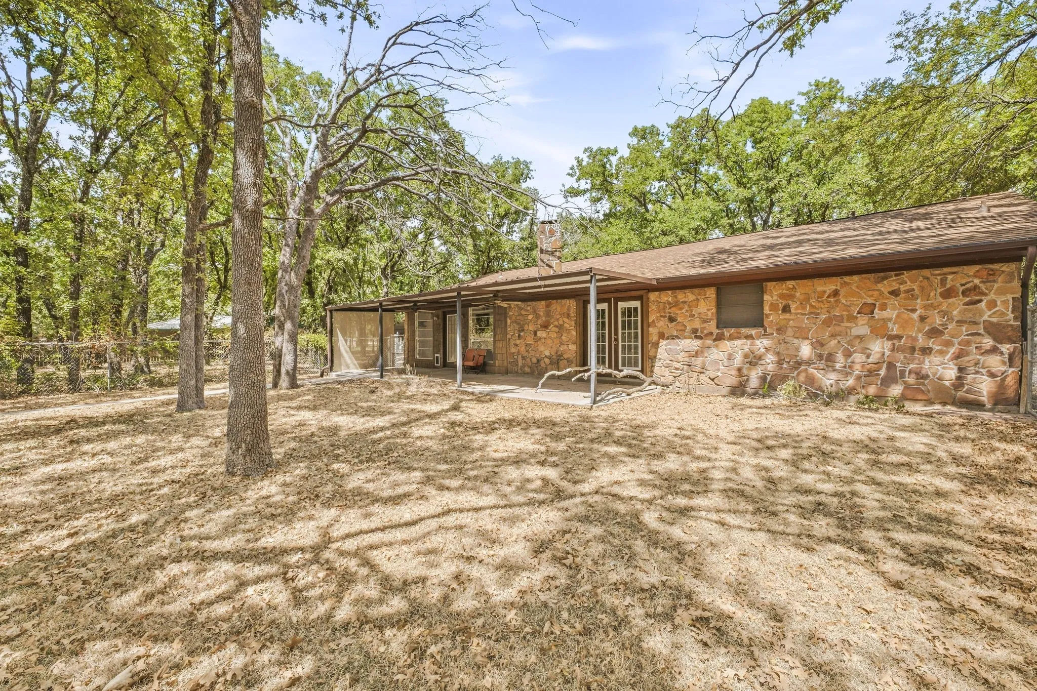 Stone exterior with a covered patio, multiple double doors, and a natural tree-lined setting