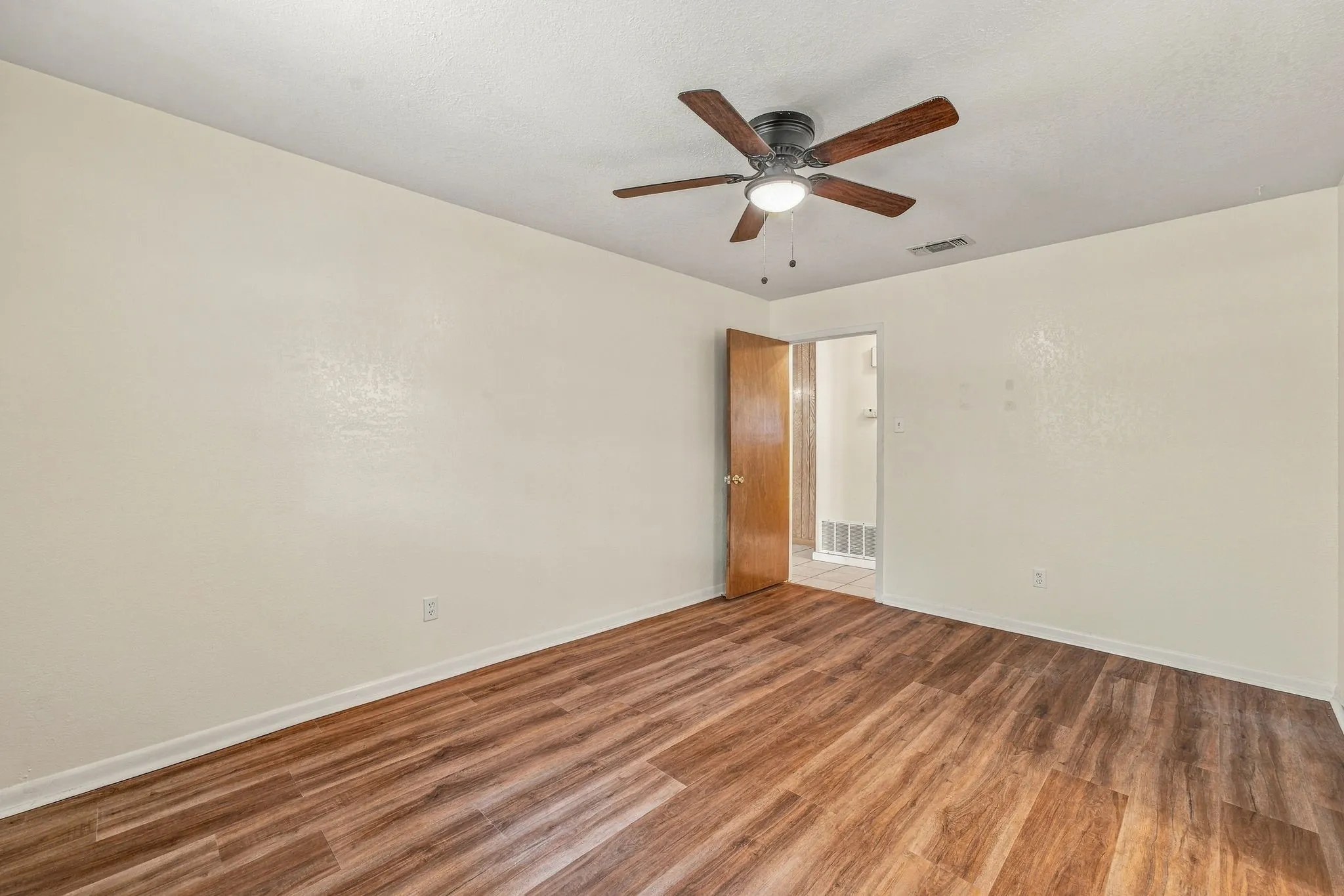 Spacious room featuring wood-finish flooring, a ceiling fan with integrated lighting, and a neutral wall finish