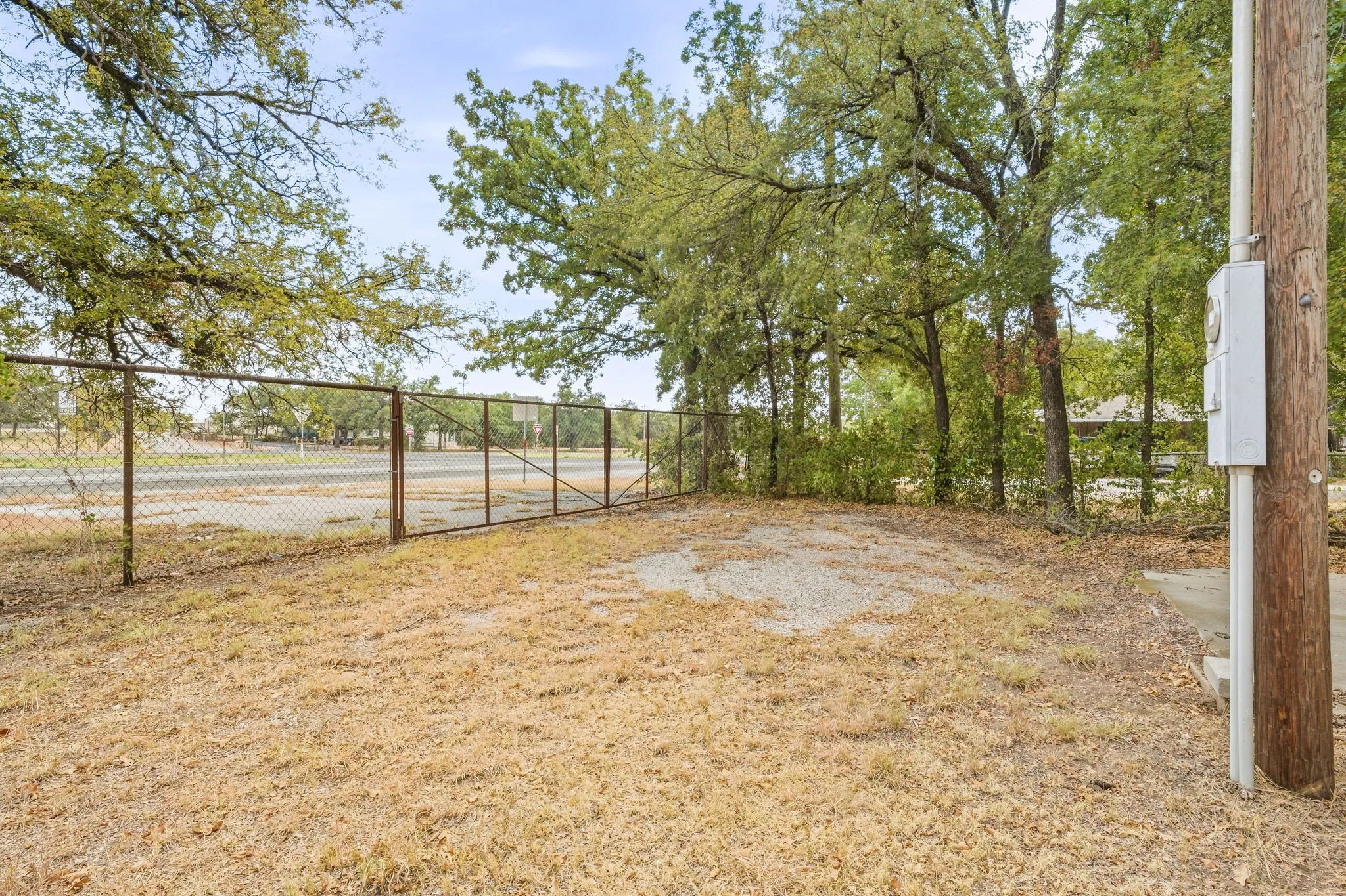 Chain-link fence with a double gate, mature trees, and a utility pole
