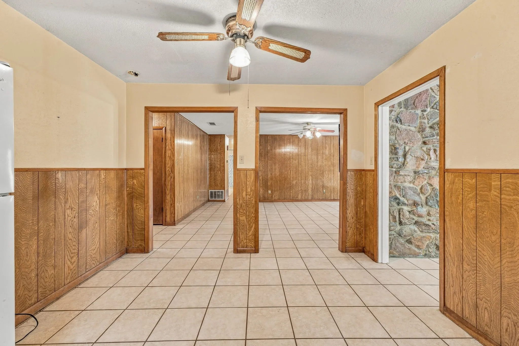 Tile flooring, wood-paneled wainscoting, and a ceiling fan with integrated lighting