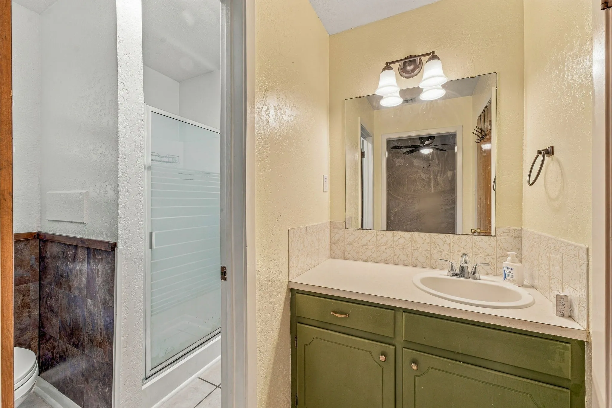 Bathroom featuring a vanity with a single sink, built-in cabinetry, wall-mounted light fixture, and a glass-enclosed shower with frosted detailing