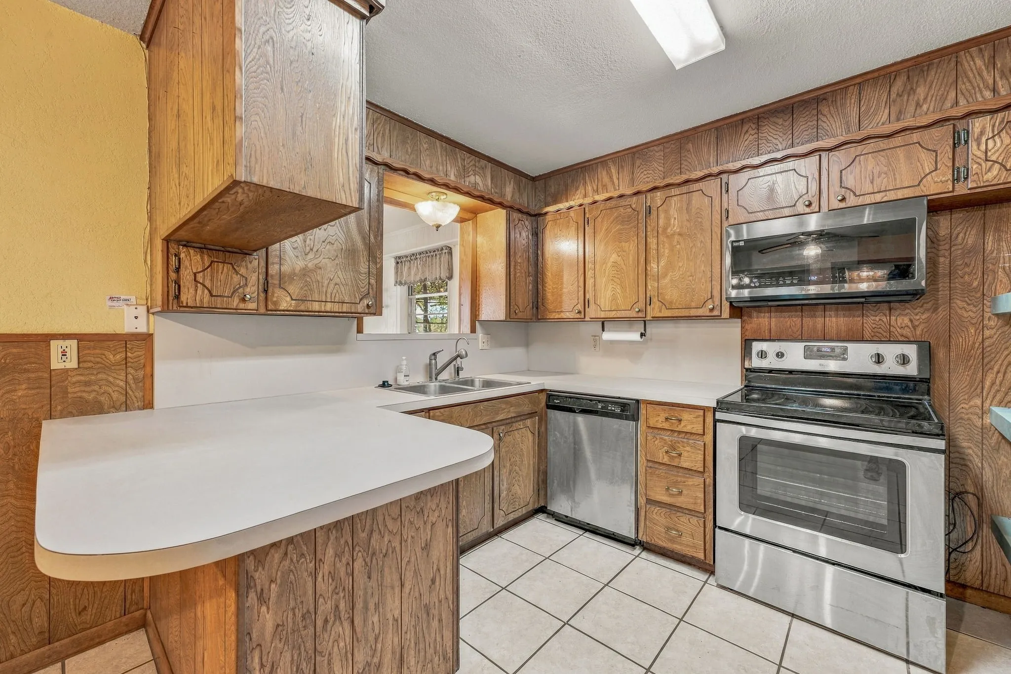Kitchen featuring wood-finish cabinetry, white countertops, a stainless steel over-the-range microwave, and a stainless steel range