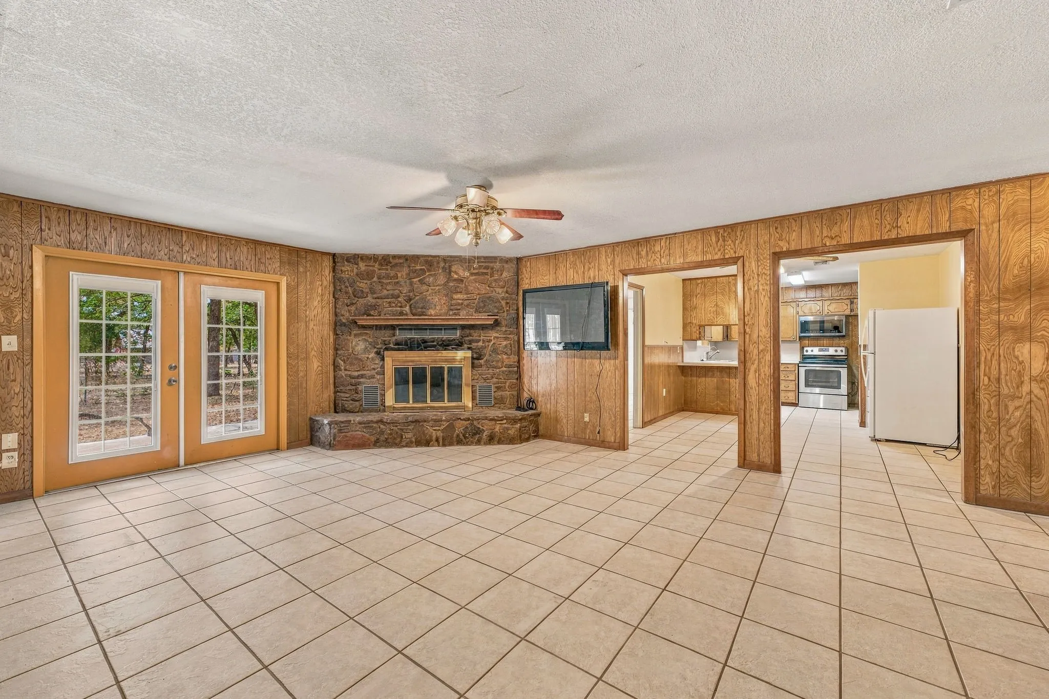 Spacious room featuring tile flooring, a stone fireplace, and double French doors