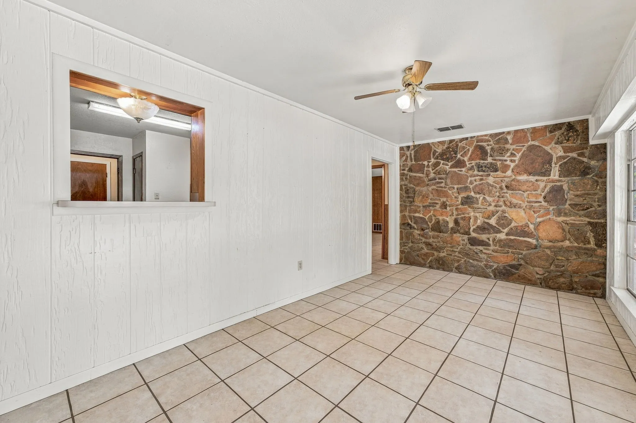 Stone accent wall, tiled flooring, built-in pass-through window, ceiling fan with integrated lighting, and white paneling