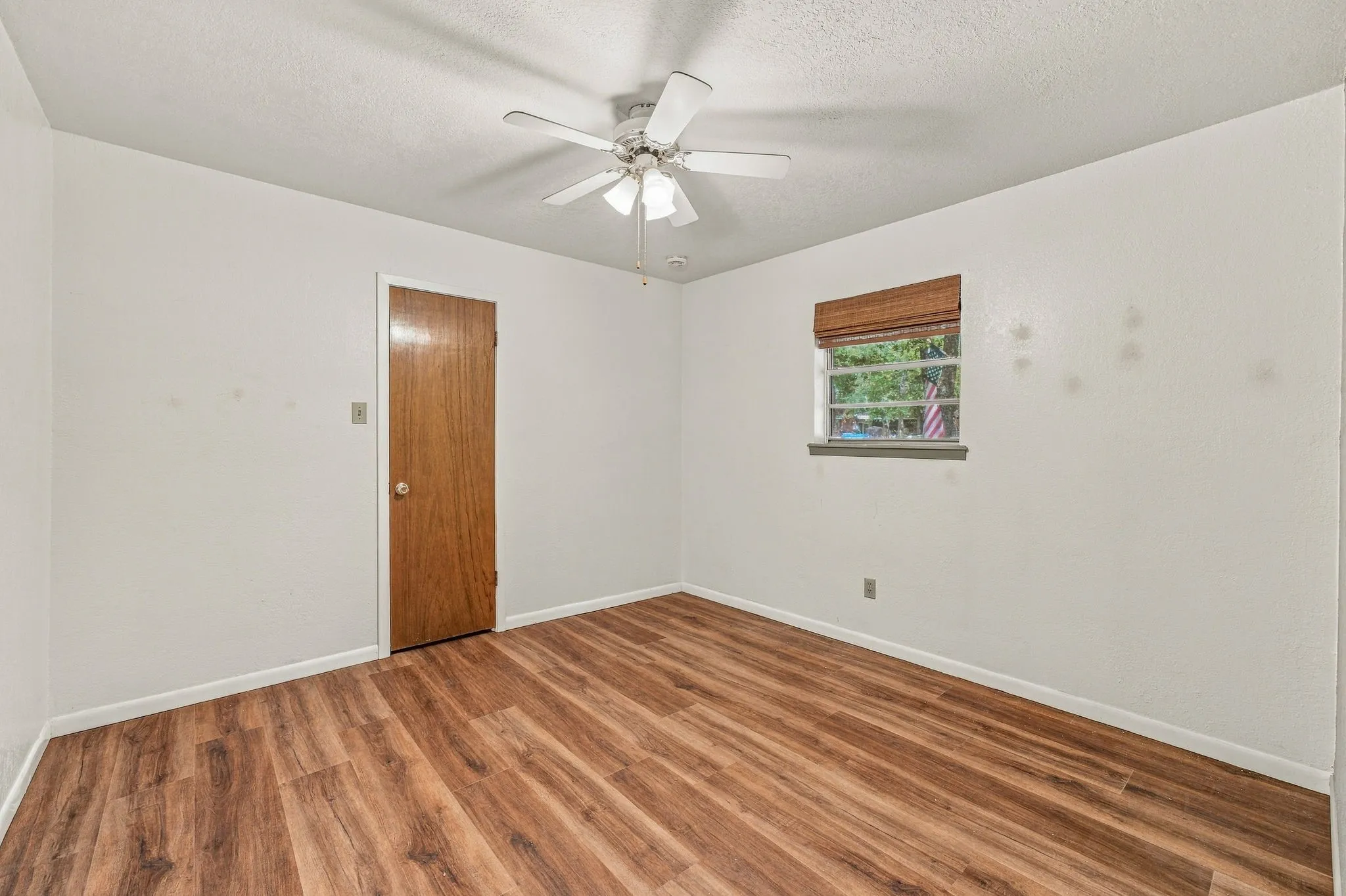 Wood-finish flooring throughout, white painted walls, and a ceiling fan with integrated lighting