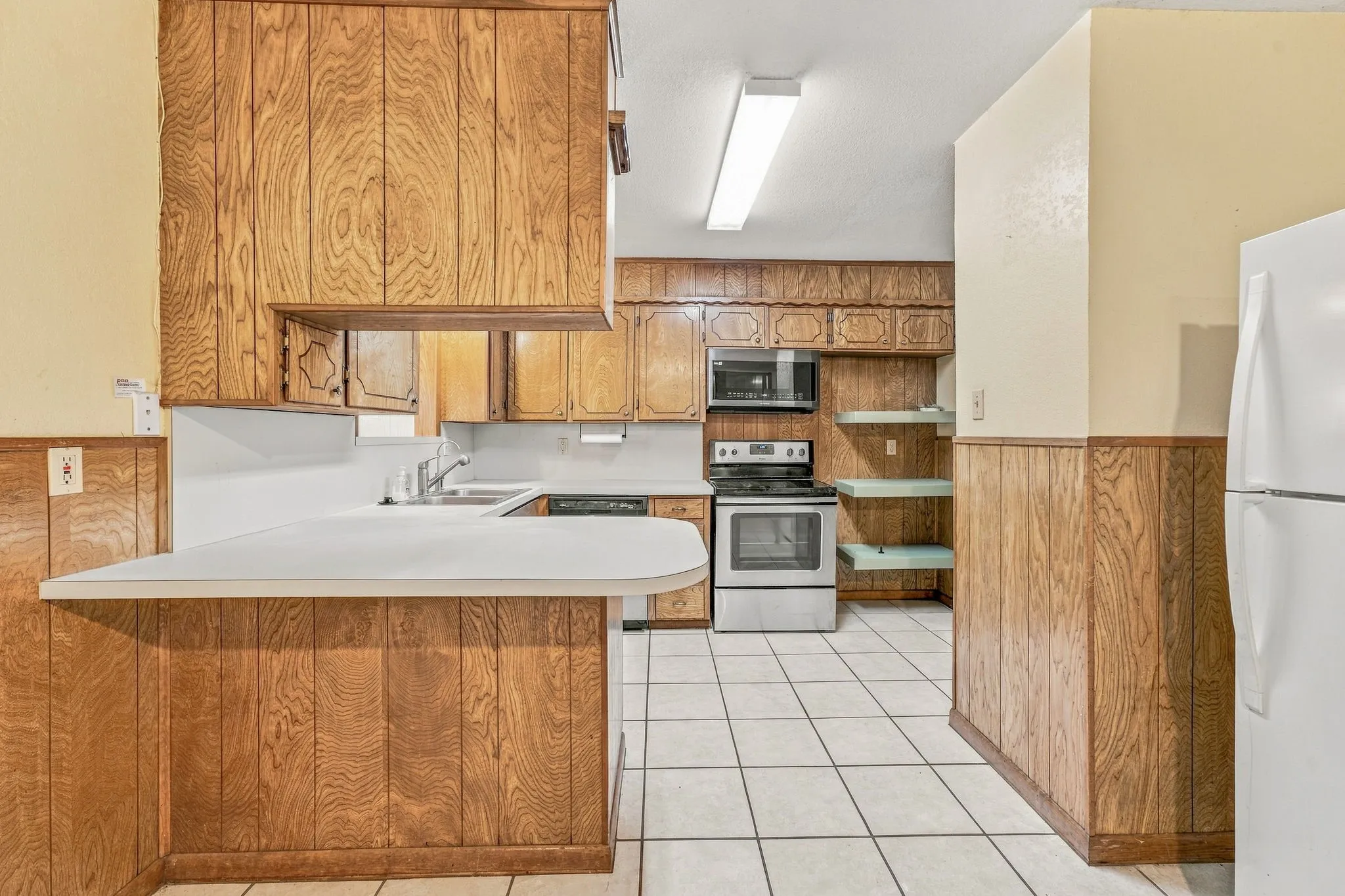 Wood-finish cabinetry and paneling, white countertop, white tile flooring, and stainless-steel appliances