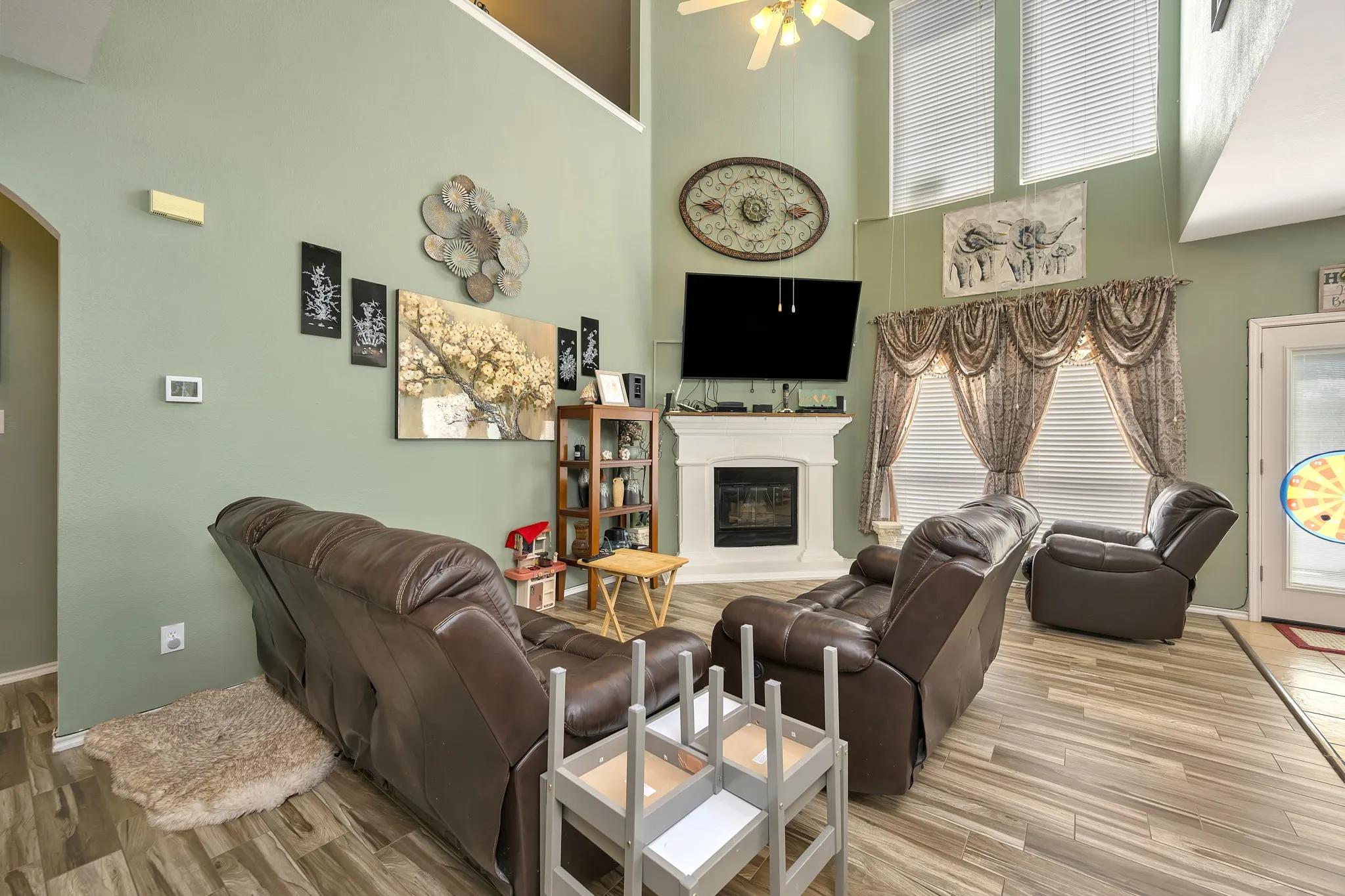 Two-story living area featuring a fireplace, wood-finish flooring, high ceilings, and multiple windows with blinds