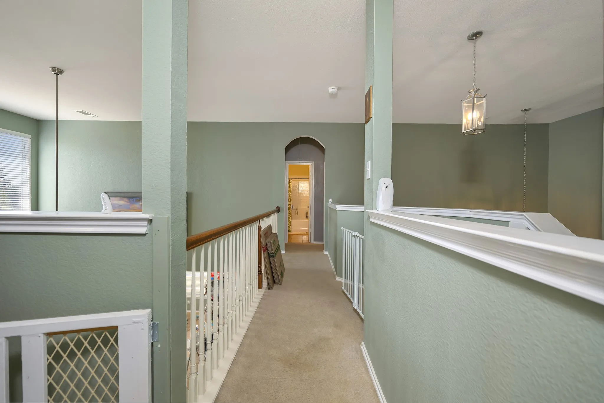 Upper-level landing with carpet flooring, light green painted walls, and white railing with wood-finish top