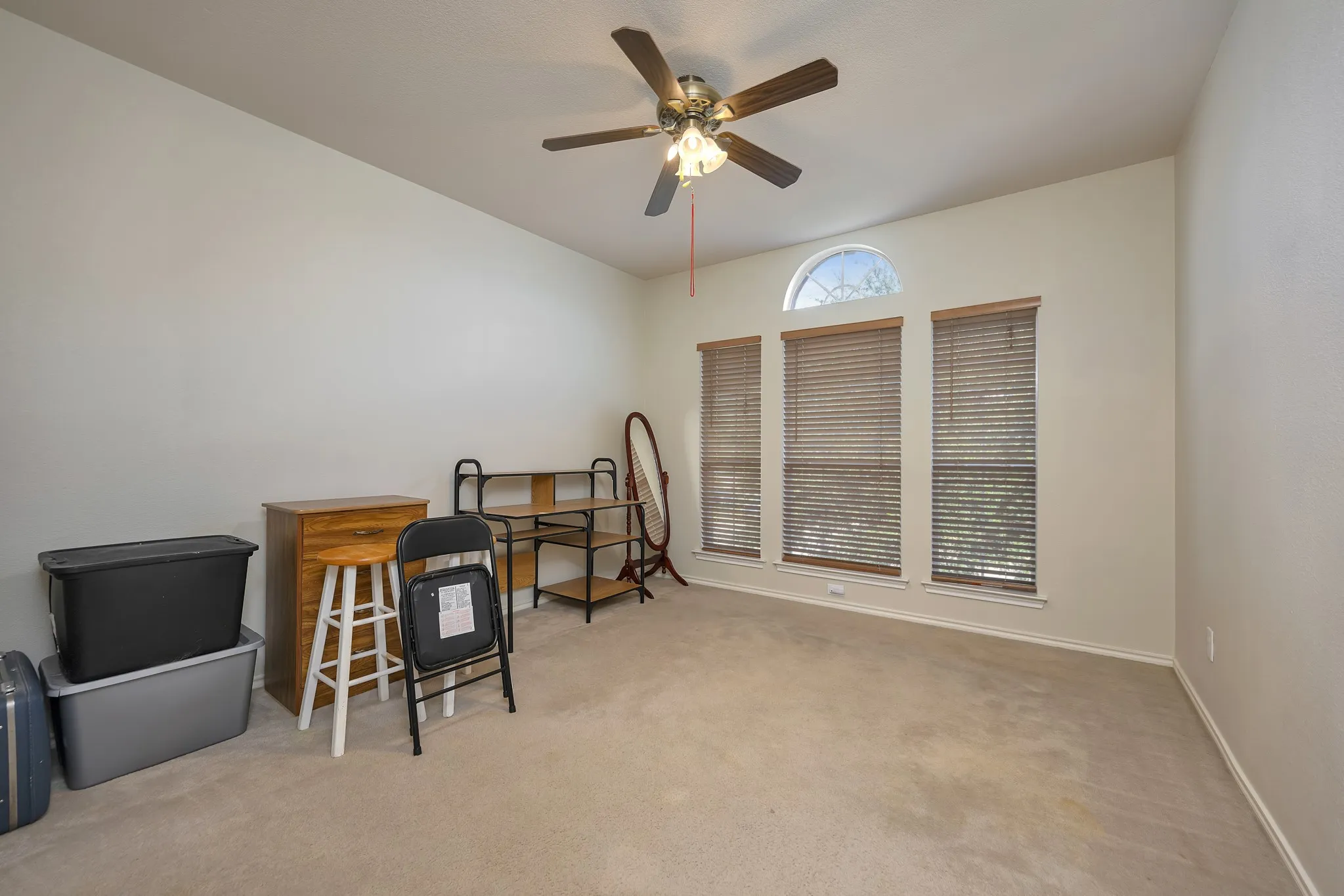 Carpeted room with a ceiling fan, arched transom window