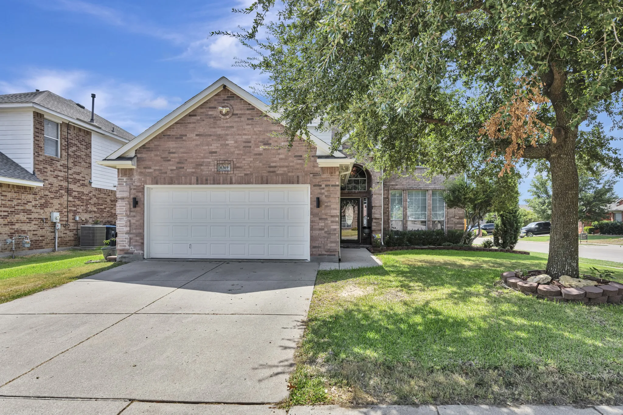 Brick facade with a two-car garage, mature front yard tree, and an arched entry