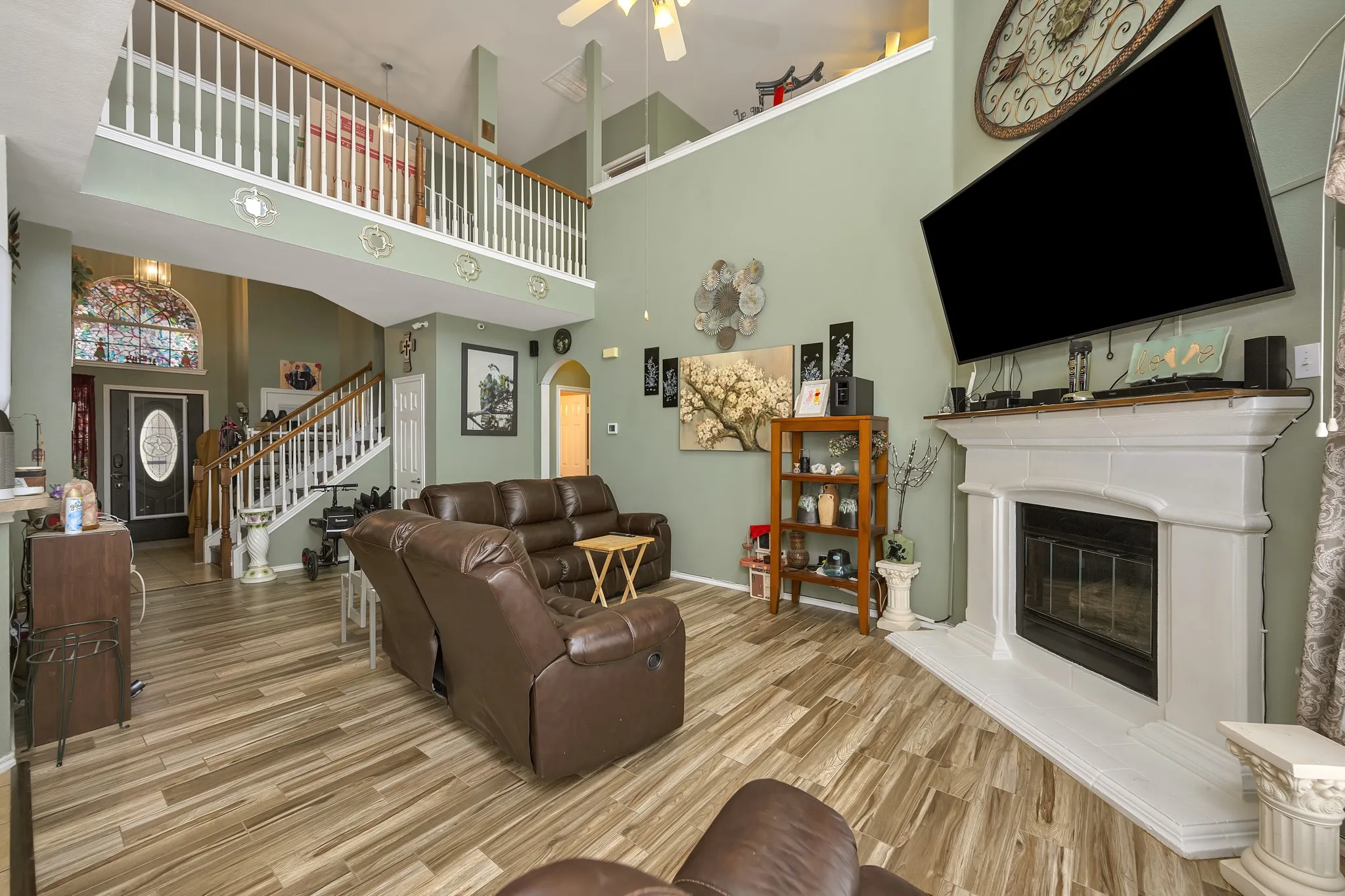 Vaulted ceiling living area featuring wood-finish flooring, a fireplace with a white mantel, and a second-story interior balcony with white railings