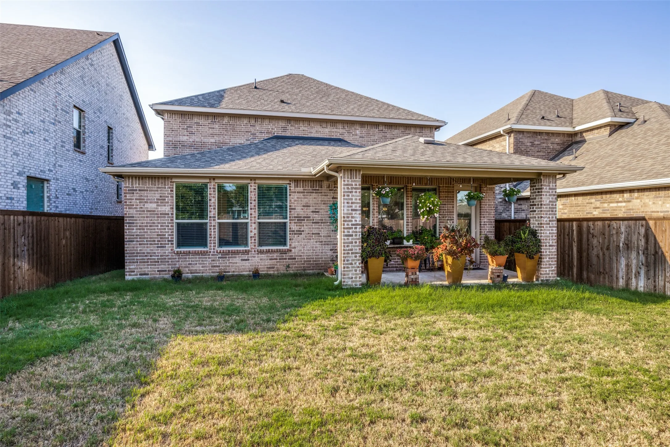 Covered patio with brick columns and a shingled roof, featuring multiple windows and a glass-paneled door