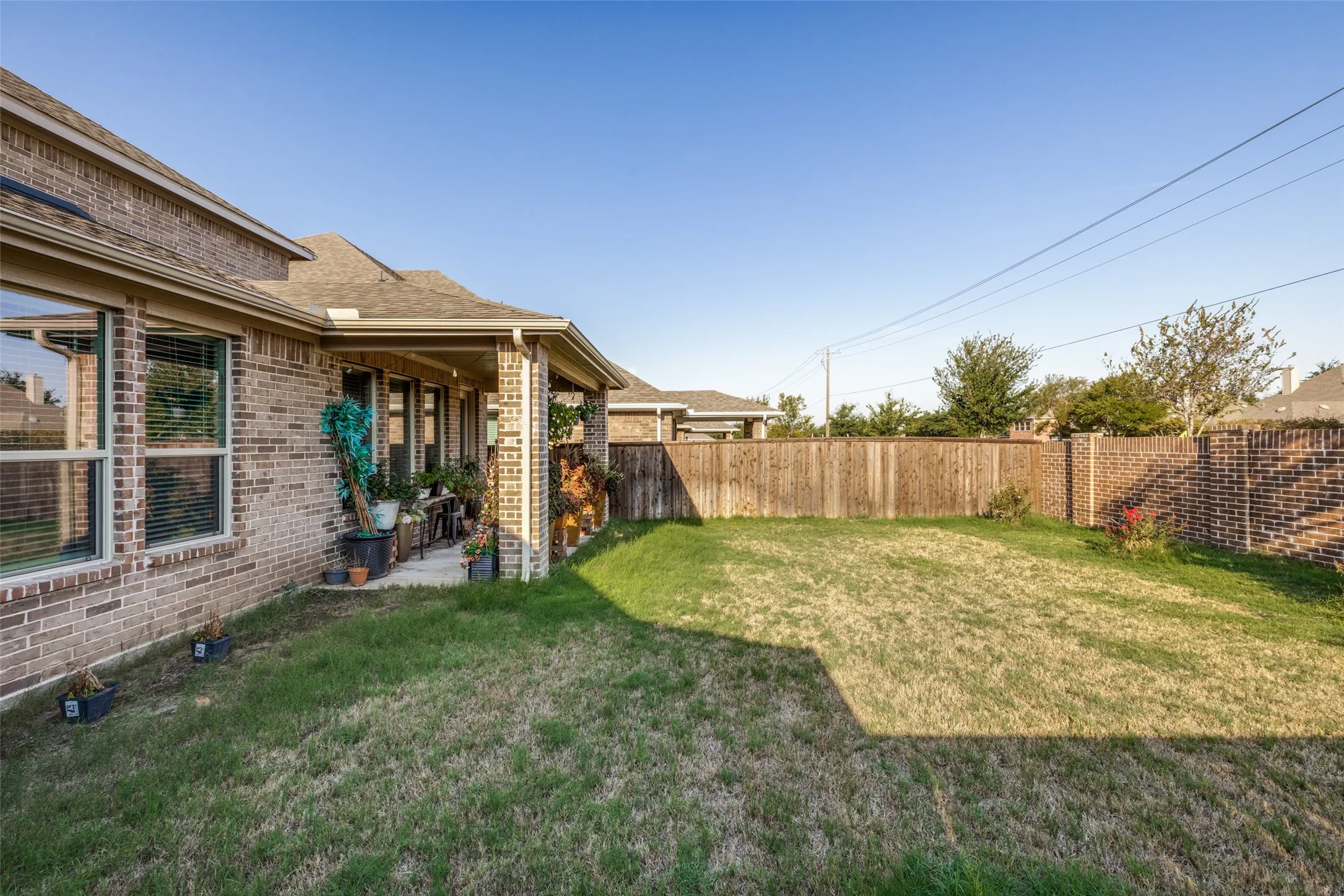 Brick exterior with a covered patio, grass area, and wood privacy fencing