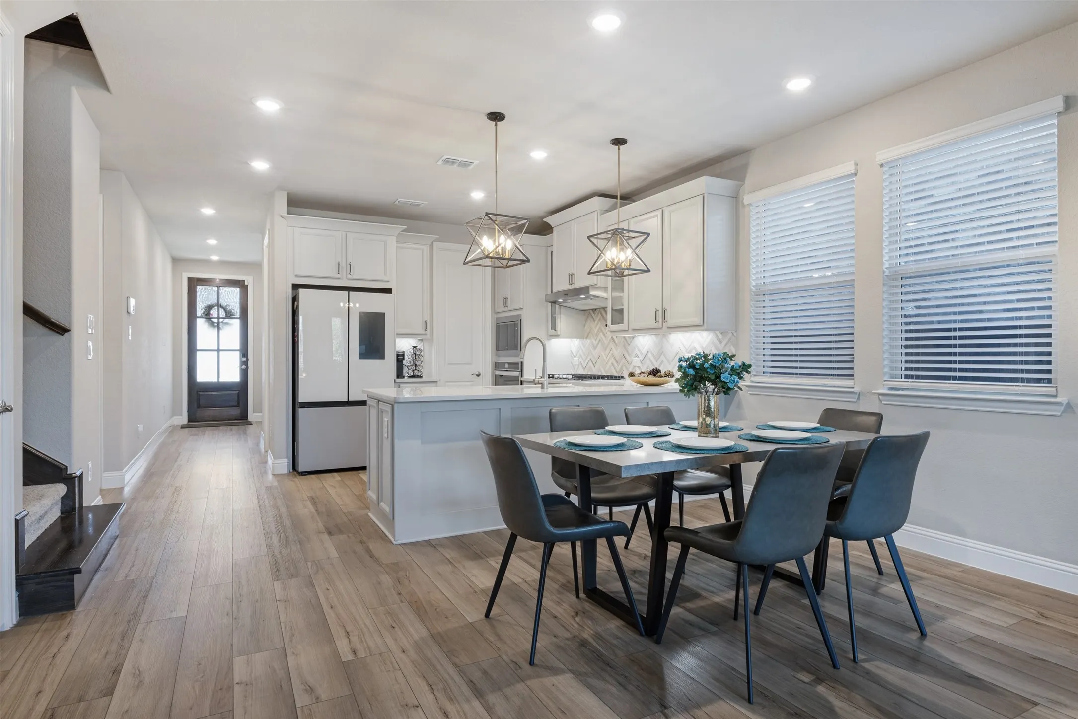 Open-concept living space featuring wood-finish flooring, recessed lighting, white cabinetry, an island with countertop seating, and a patterned tile backsplash