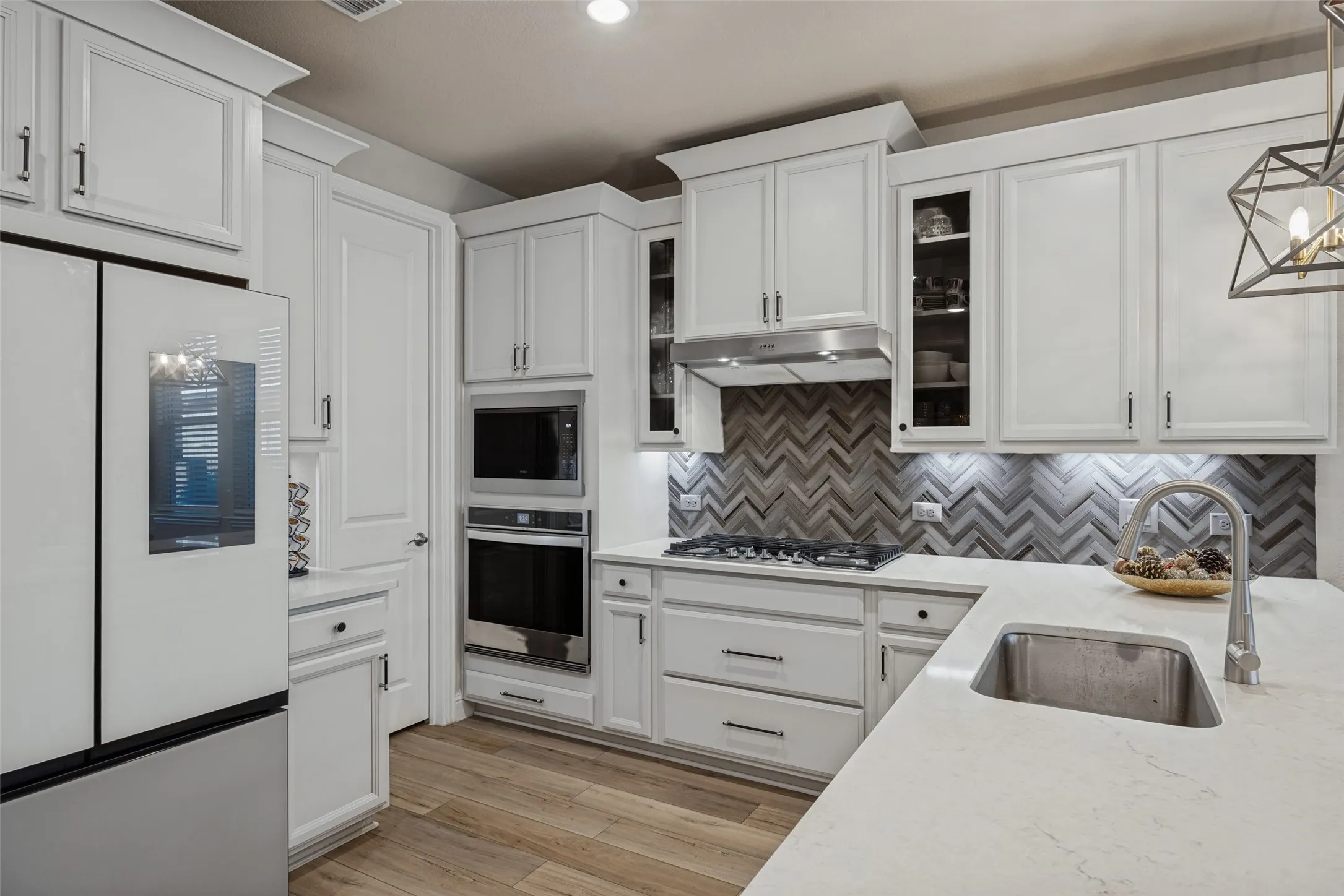 White cabinetry with crown molding, chevron tile backsplash, stainless steel appliances, wood-finish flooring, and a kitchen island with an undermount sink