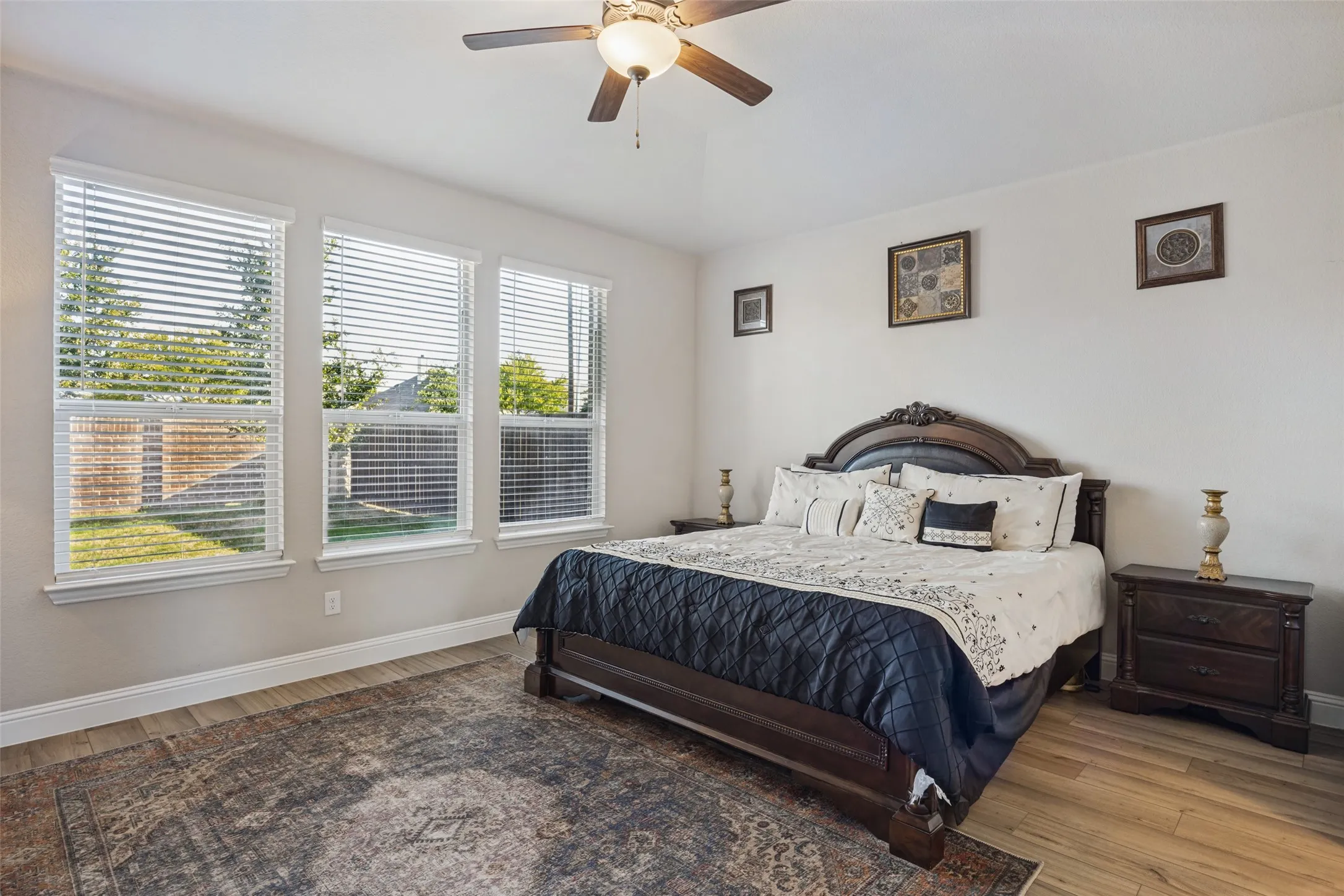 Wood-finish flooring, multiple windows with blinds, ceiling fan with integrated lighting, and a neutral wall color