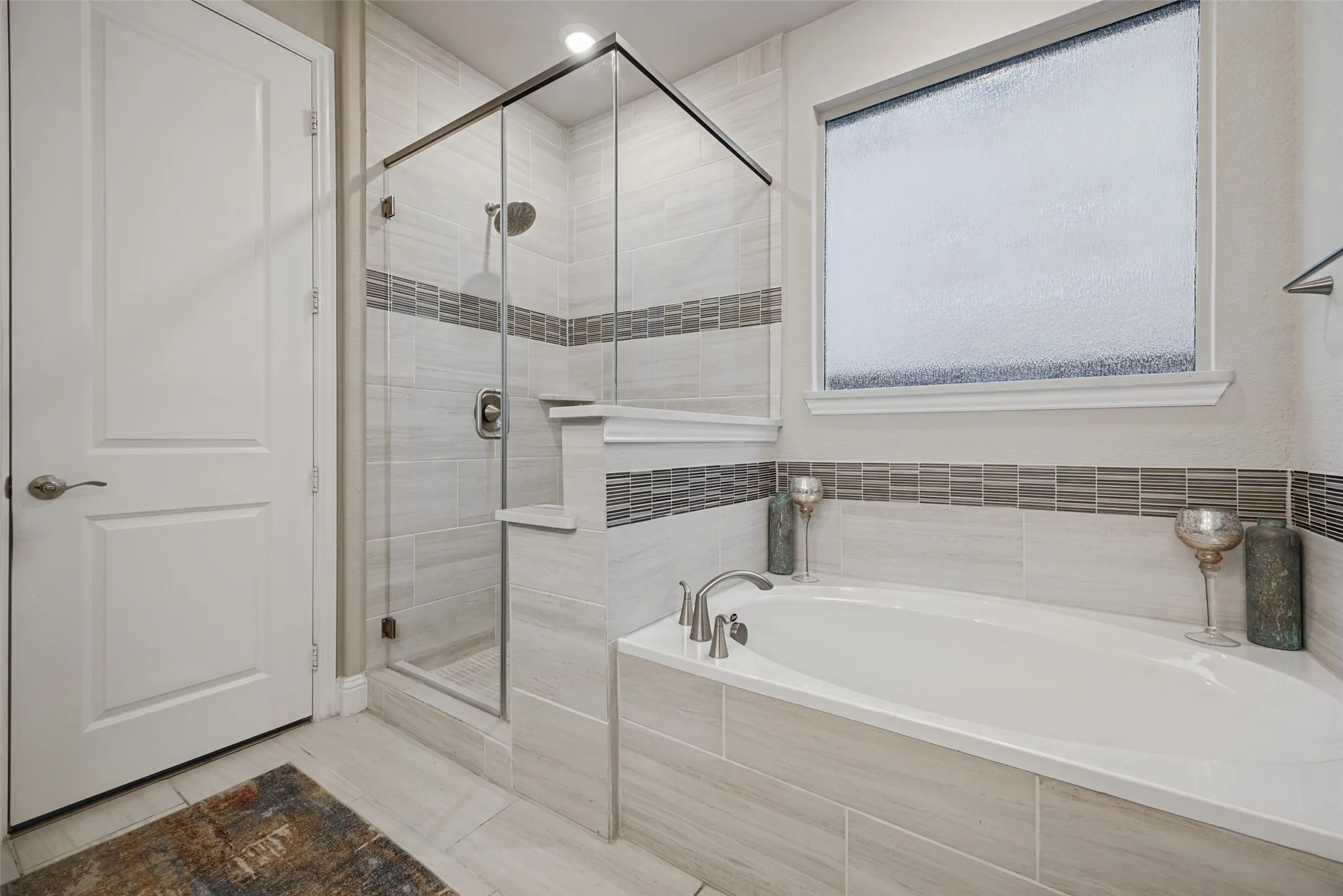 Built-in bathtub with deck-mounted faucet, glass-enclosed shower with tile surround, and privacy window