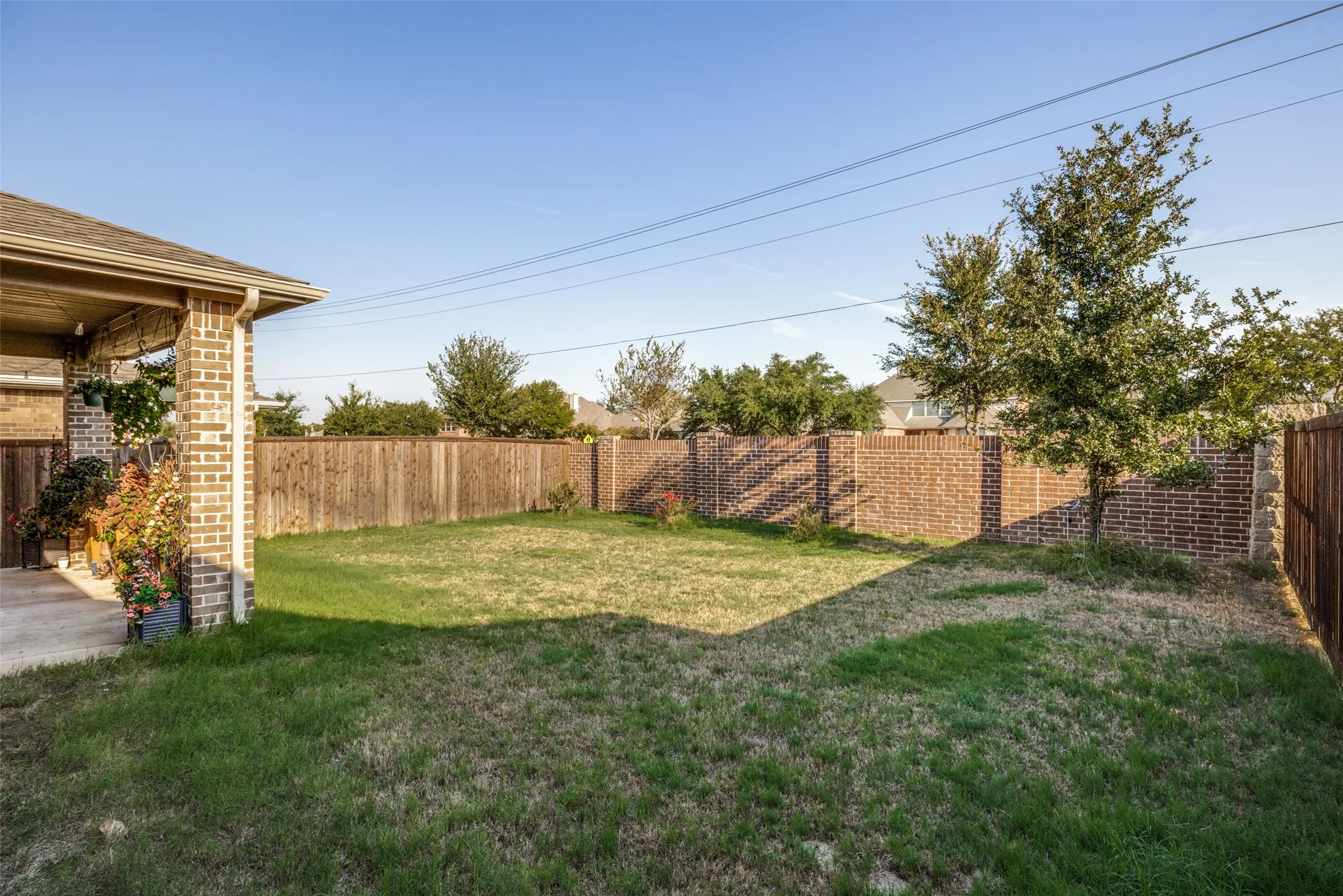 Expansive lawn area featuring a covered concrete patio, brick exterior, and a combination of brick and wood privacy fencing