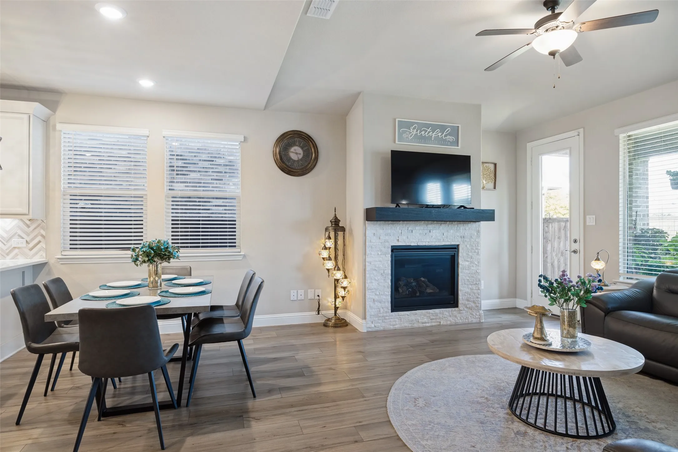Wood-finish flooring throughout, featuring a stone-clad fireplace with a dark wood mantel, recessed lighting, and a ceiling fan