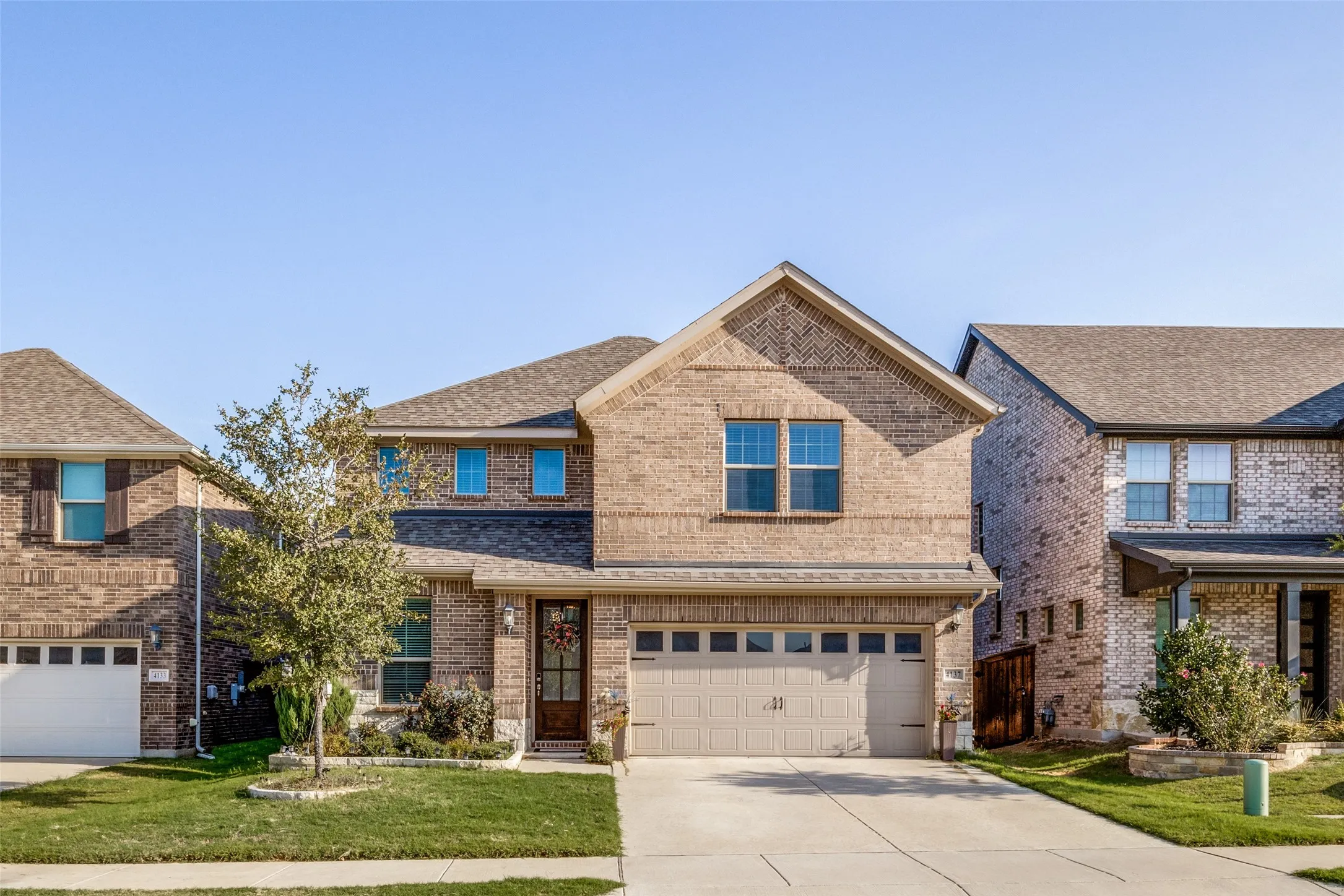 Two-story brick exterior with an attached two-car garage, mature landscaping, and a covered front entry