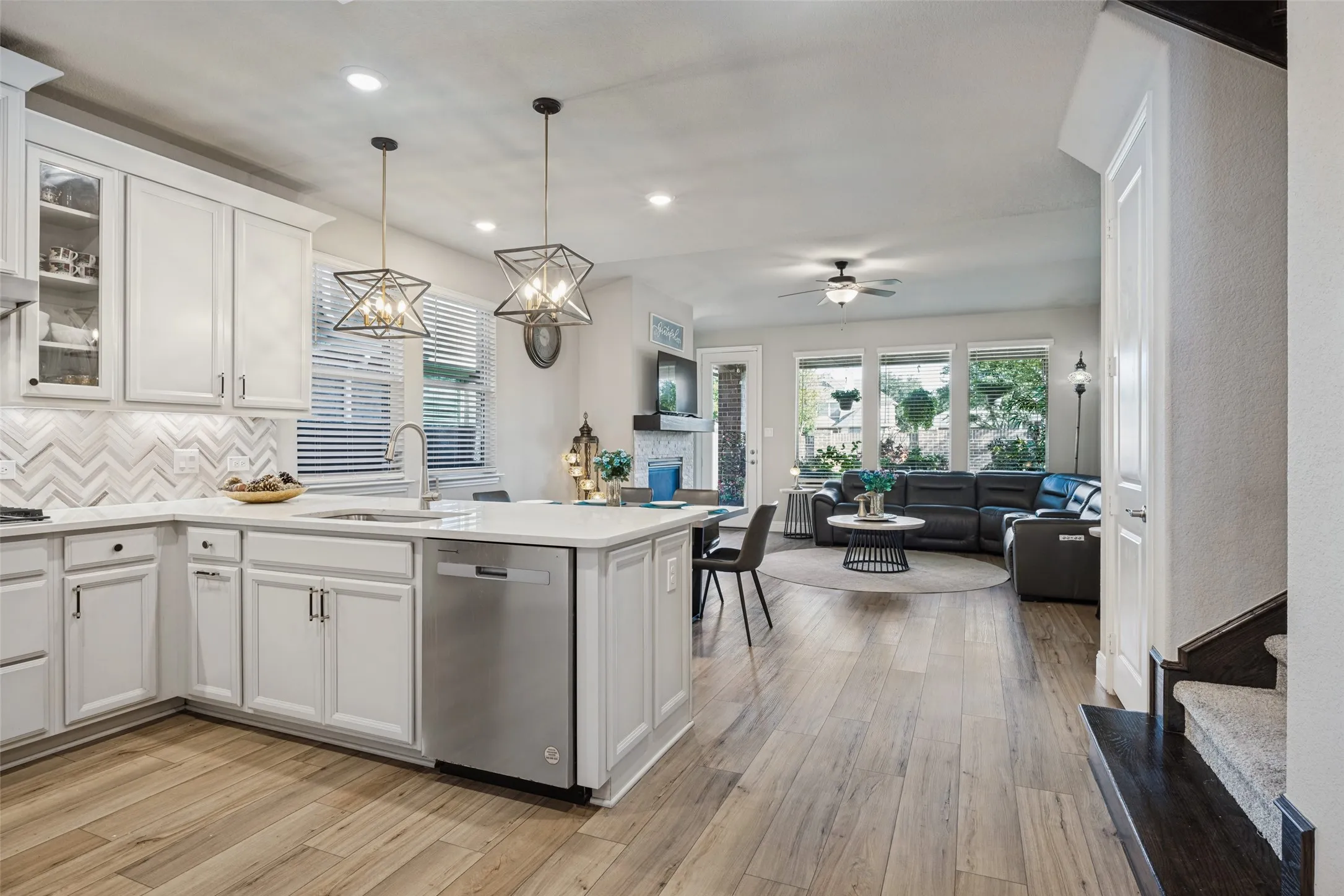 White kitchen cabinetry, herringbone tile backsplash, stainless steel dishwasher, wood-finish flooring, and multiple windows