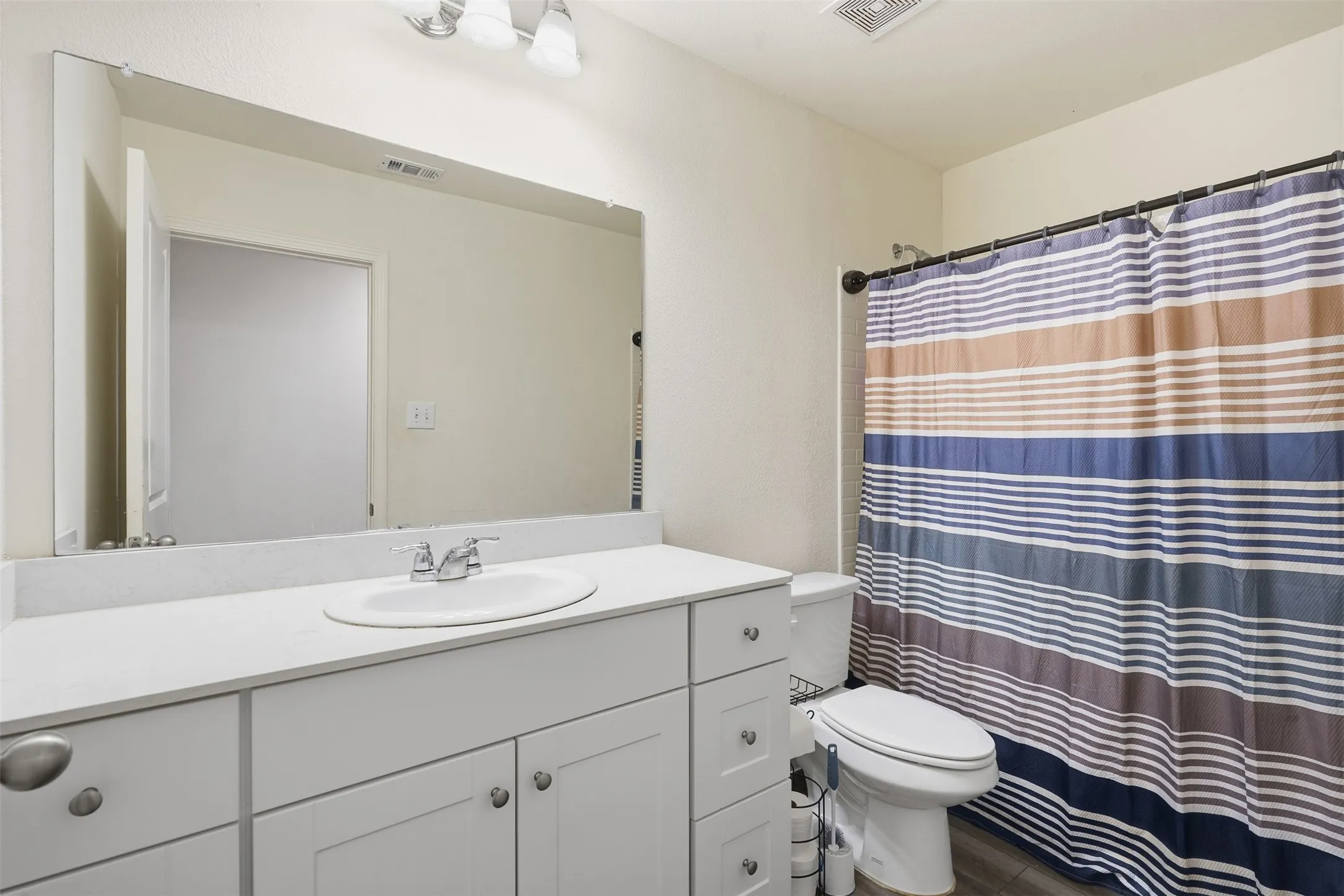 White vanity with cabinet storage, large mirror, and shower with a dark rod