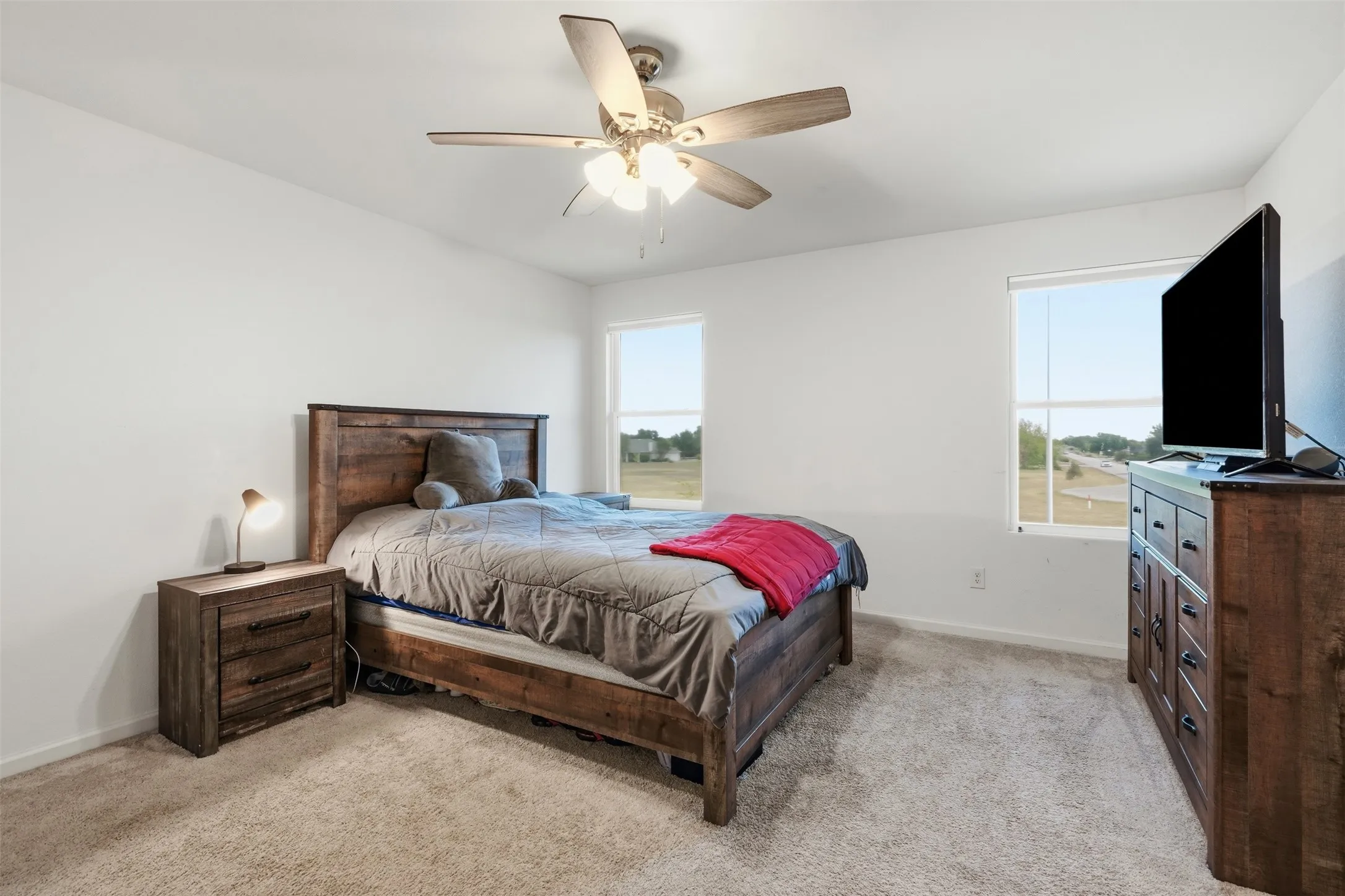 Carpeted room with a ceiling fan, two windows, and white walls