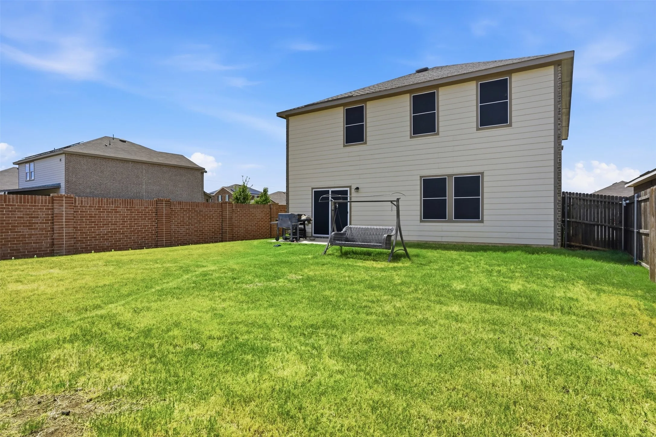 Expansive green lawn, durable brick perimeter fencing, and a two-story exterior with siding