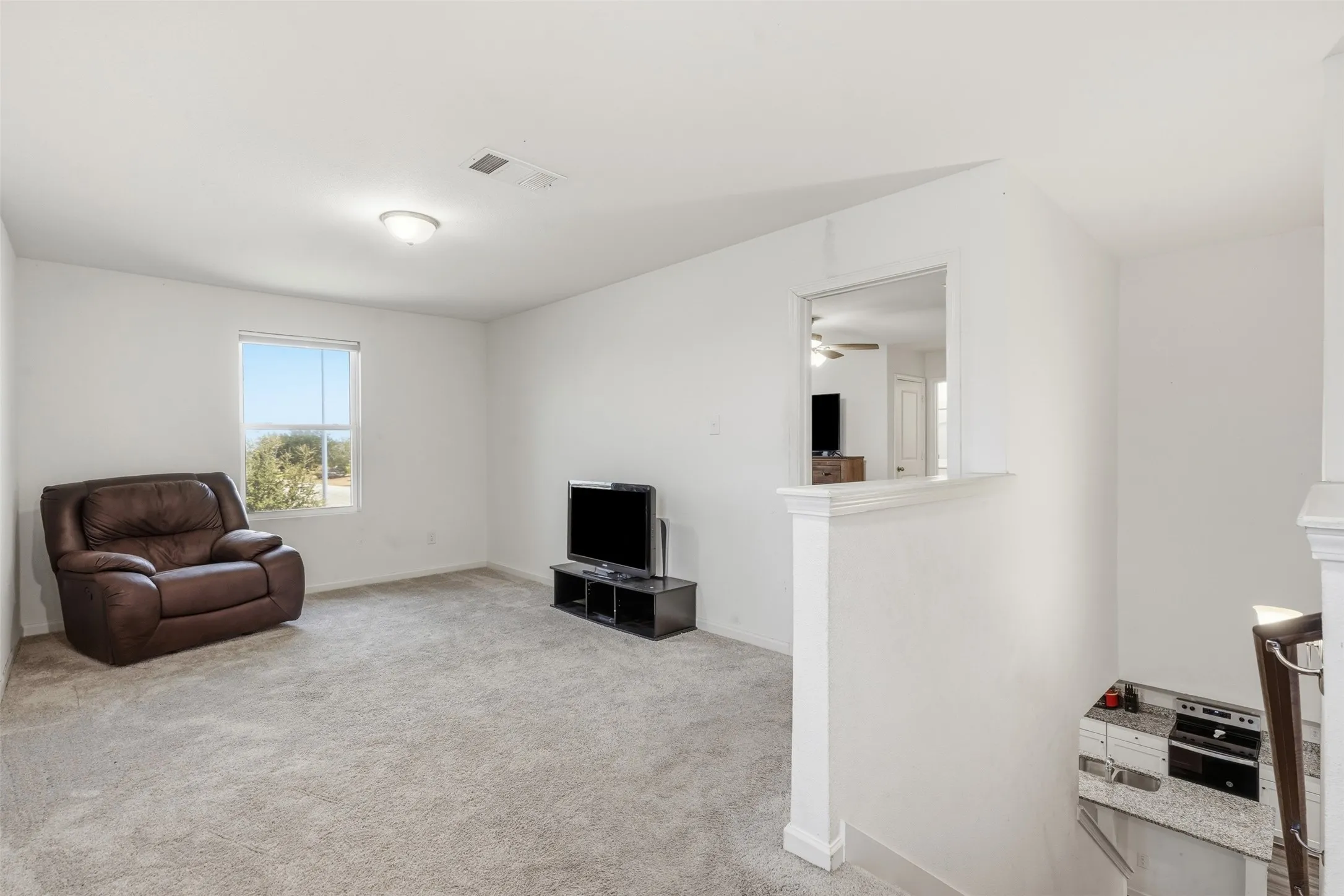 Spacious room featuring carpeting, natural light from a window, and a built-in half wall with a window-style opening