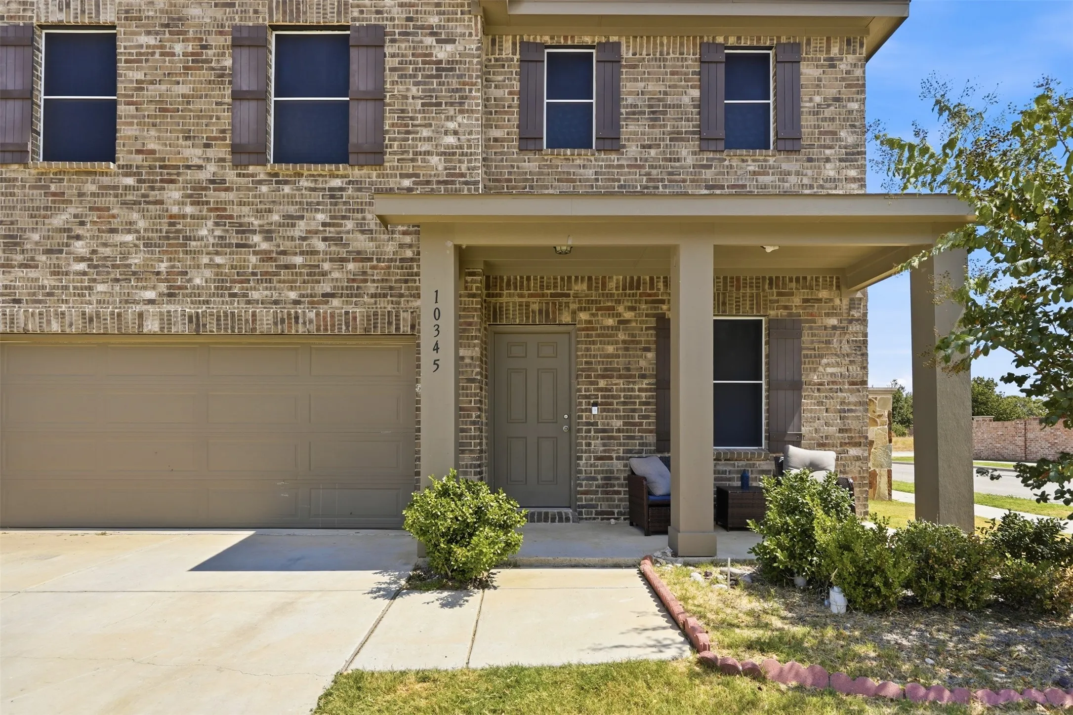 Brick facade with decorative shutters, covered front porch, concrete driveway, and attached garage