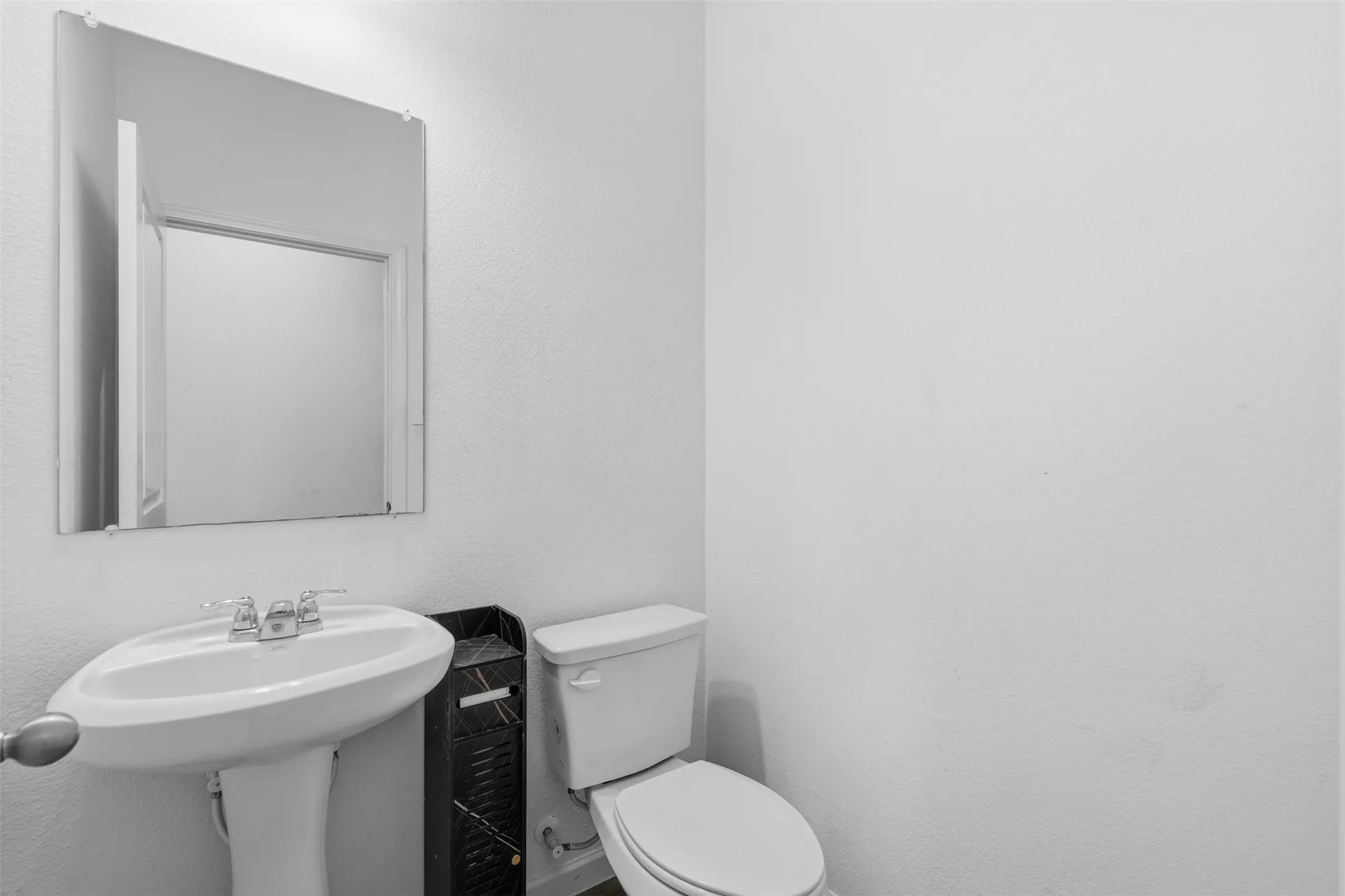 Pedestal sink with chrome fixtures and a wall-mounted mirror