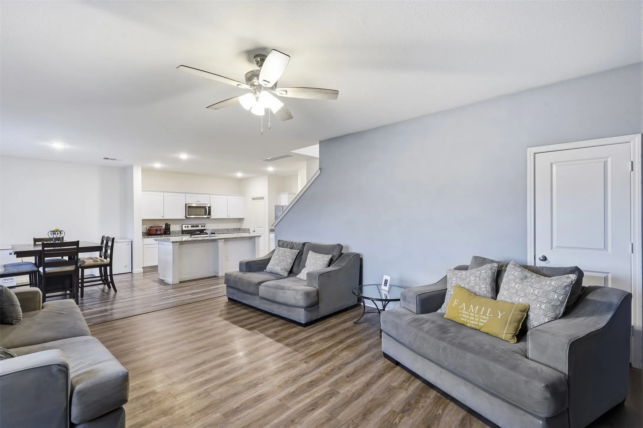 Open-concept living area featuring wood-finish flooring, a ceiling fan with light, recessed lighting, white kitchen cabinetry, and an island with a countertop