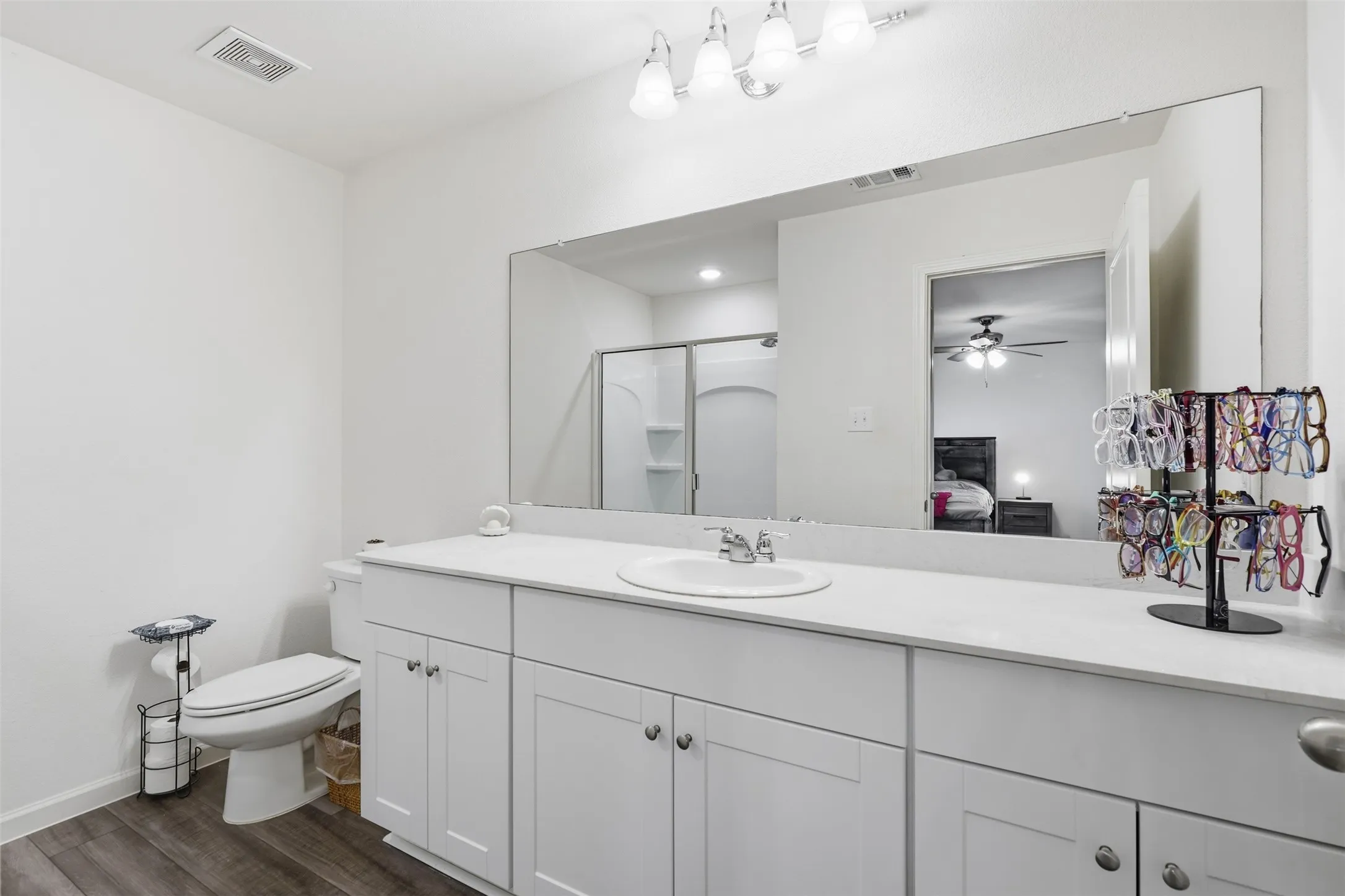 White vanity with integrated sink, expansive mirror, wood-finish flooring, and a shower enclosure
