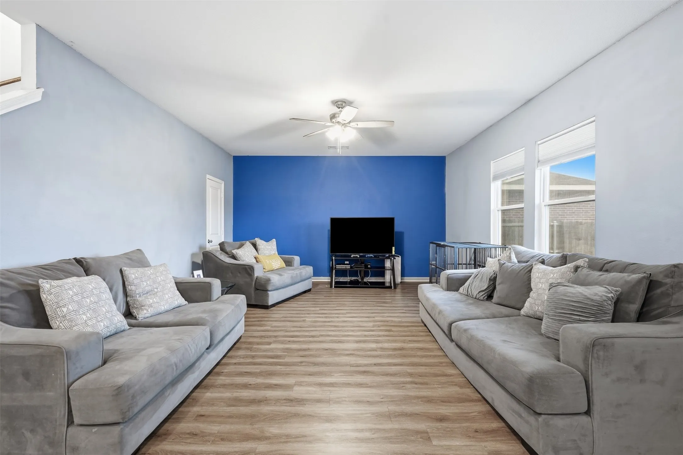 Spacious living area featuring wood-finish flooring, a vaulted ceiling, and multiple windows with roller shades