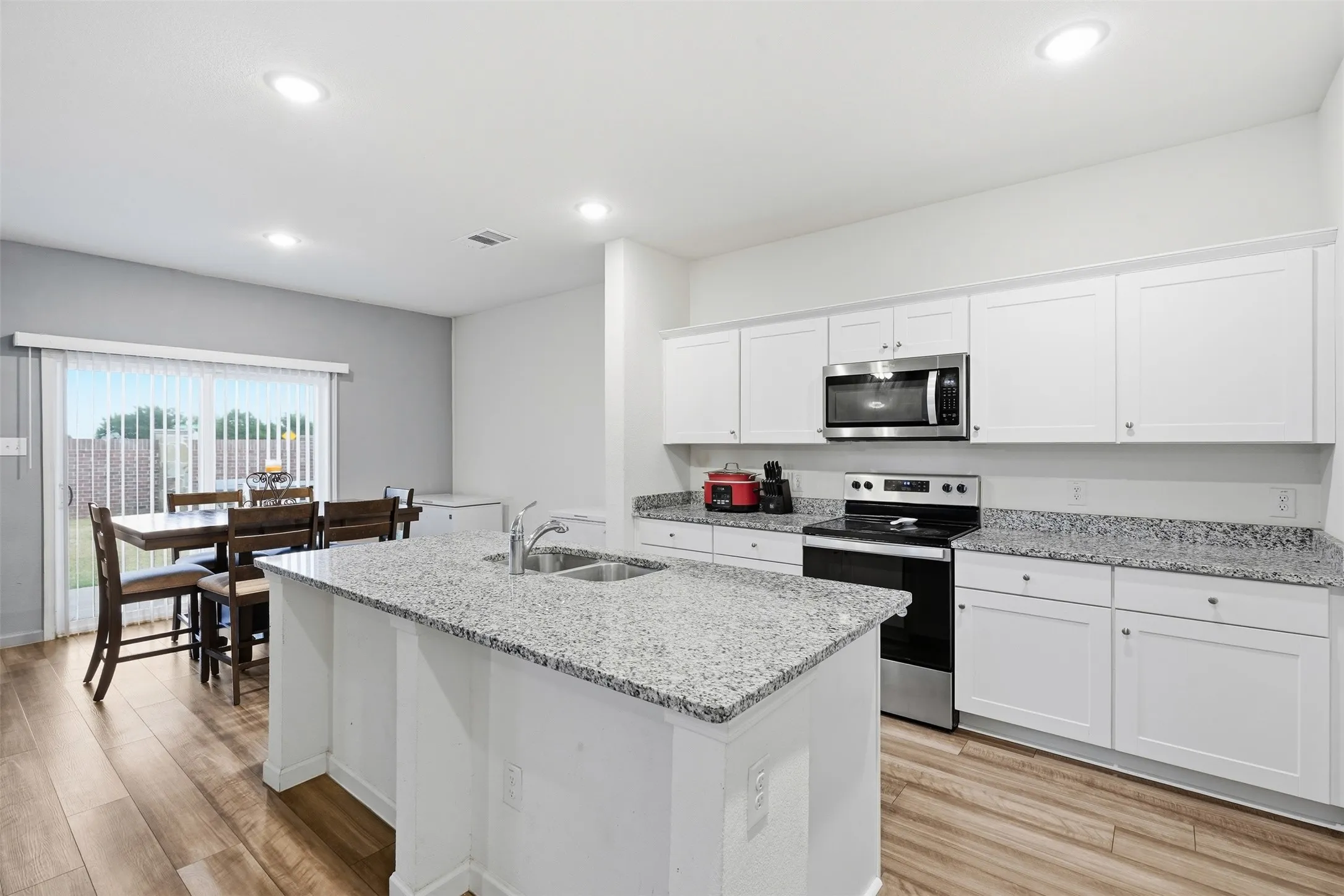 Kitchen with white cabinetry, granite countertops, stainless steel appliances, wood-finish flooring, and recessed lighting