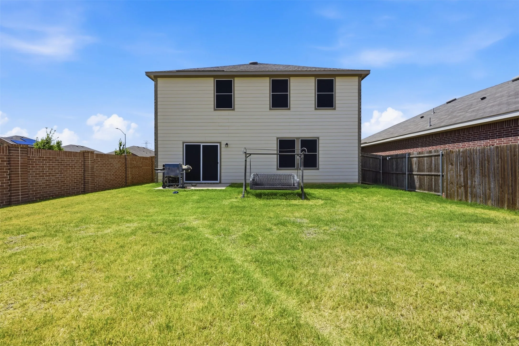 Expansive lawn area, private patio, sliding glass door access, and a durable brick fence