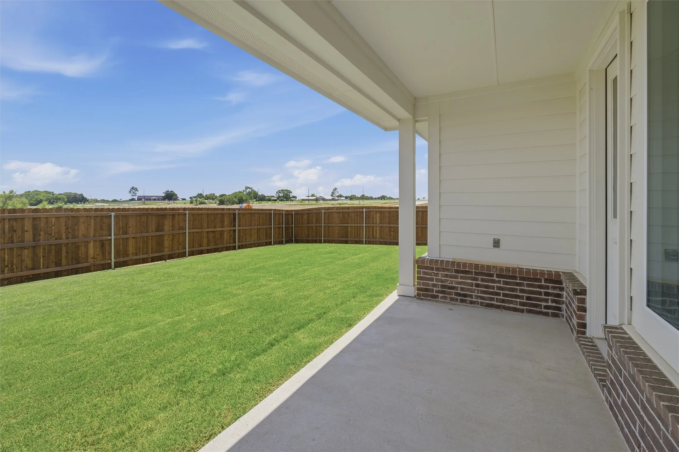 Covered concrete patio opening to a private backyard with a newly installed wood fence