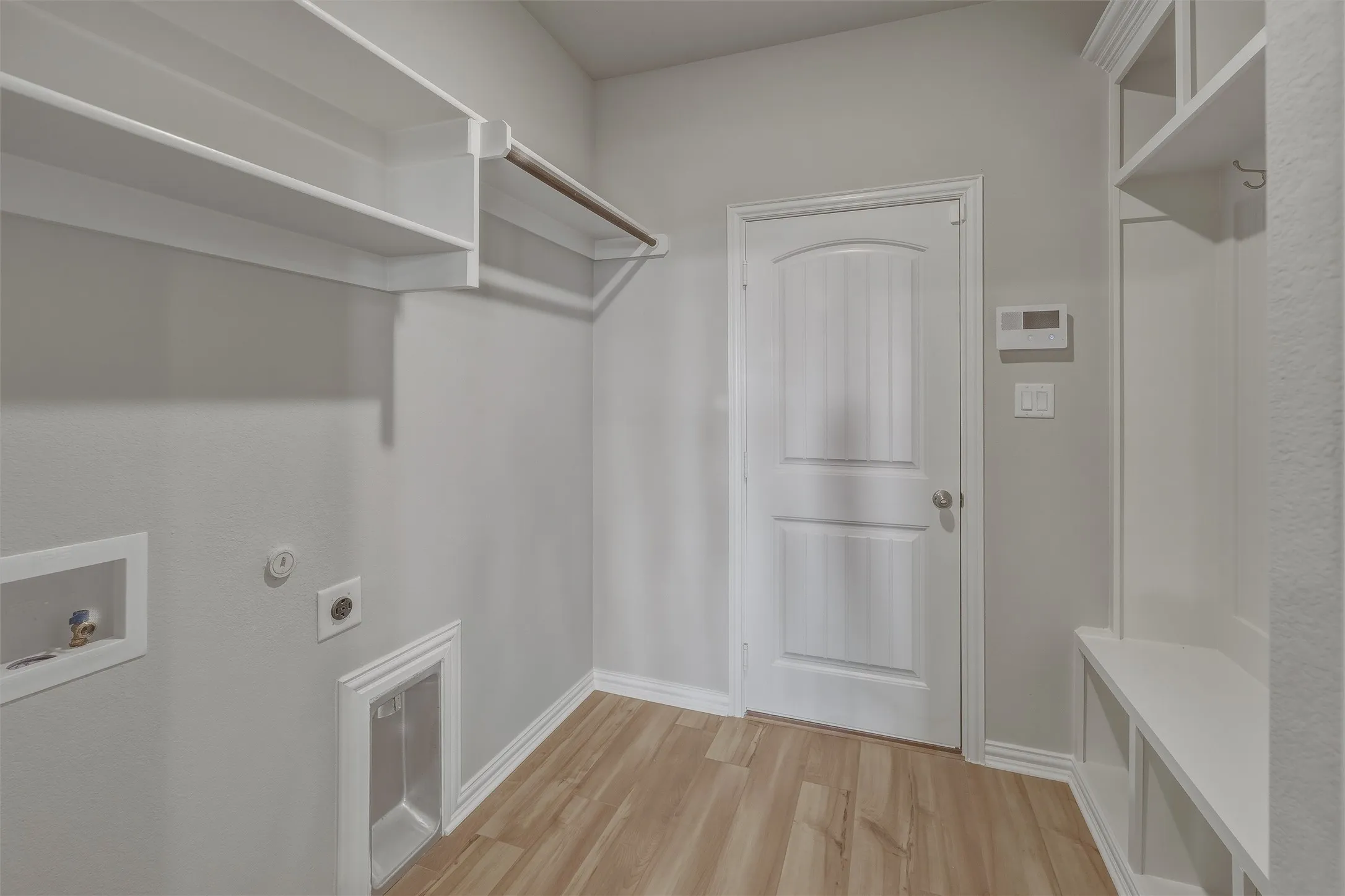 Dedicated laundry area featuring wood-finish flooring, built-in shelving, a hanging rod, and utility hookups