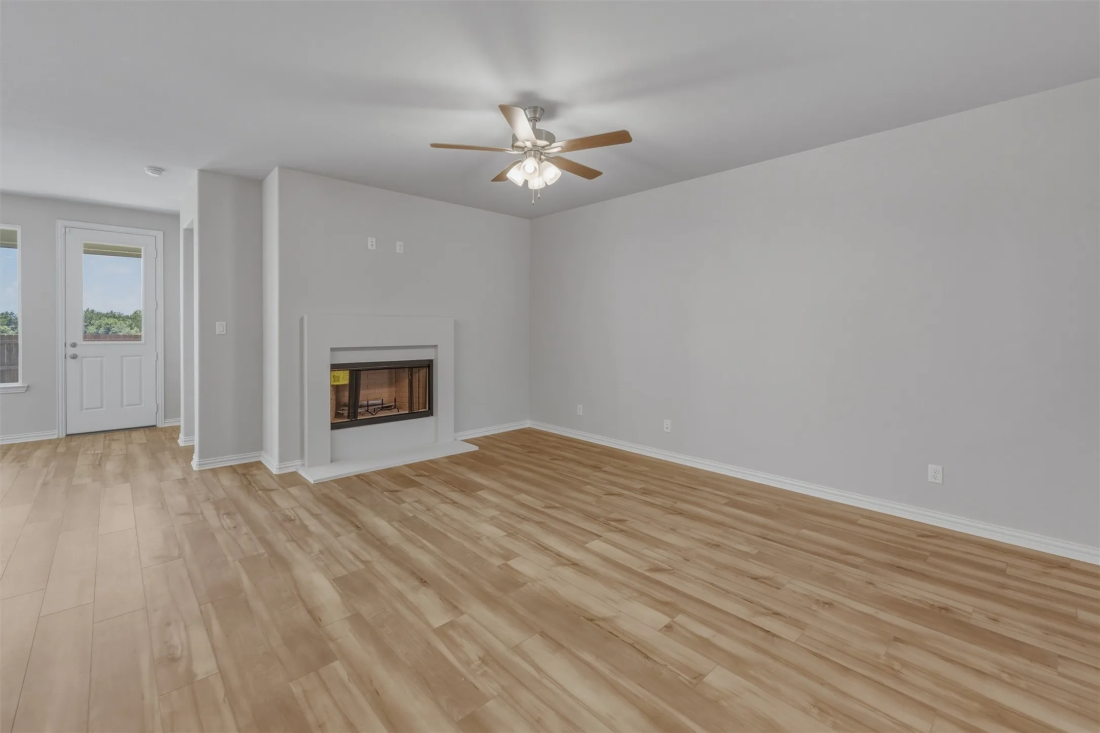 Spacious living area featuring light wood-finish flooring, a white mantel fireplace, and a ceiling fan with integrated lighting