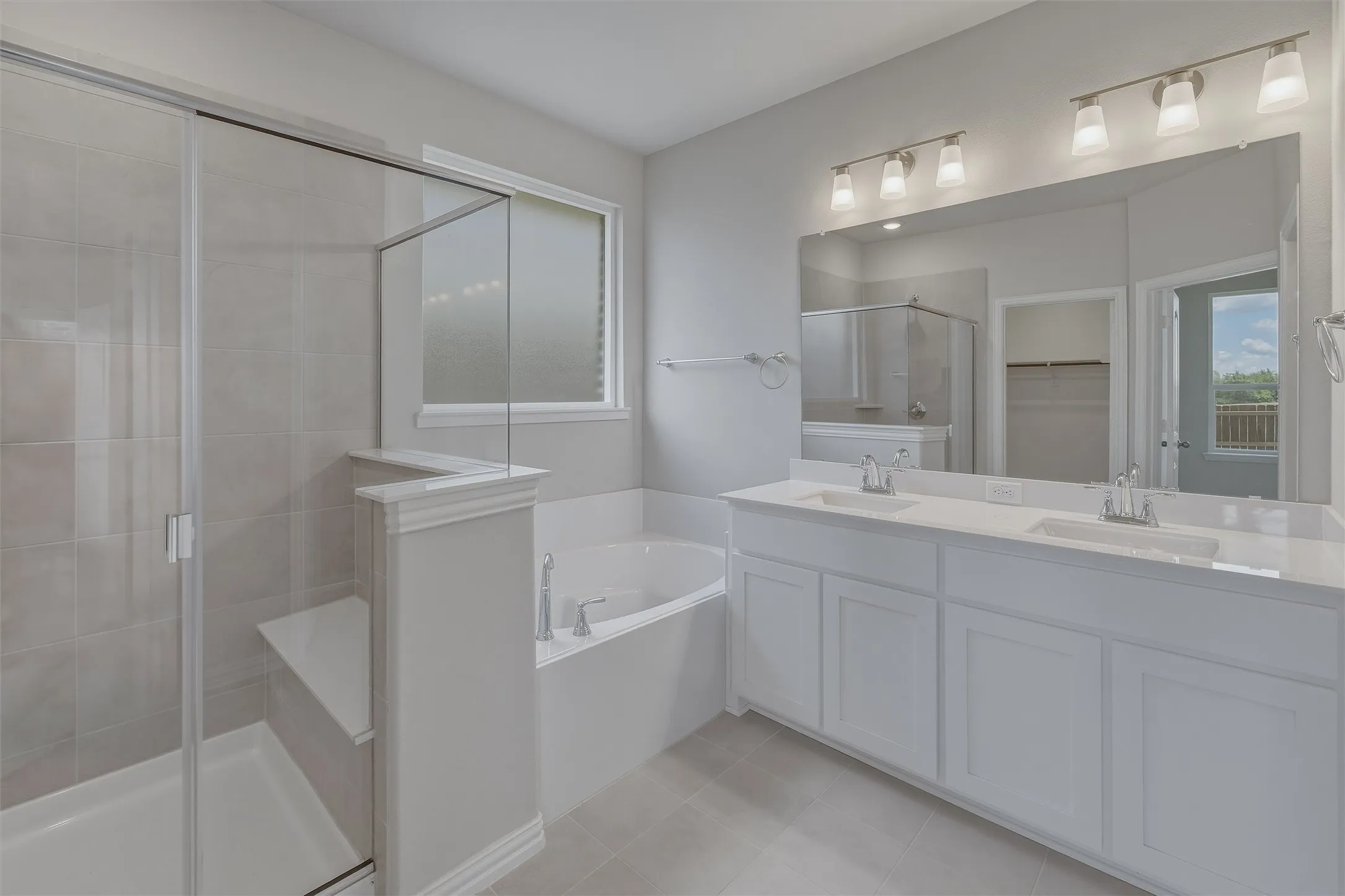 Bathroom featuring a dual vanity with white cabinetry and integrated sinks, a built-in garden tub, and a separate glass-enclosed shower with a bench