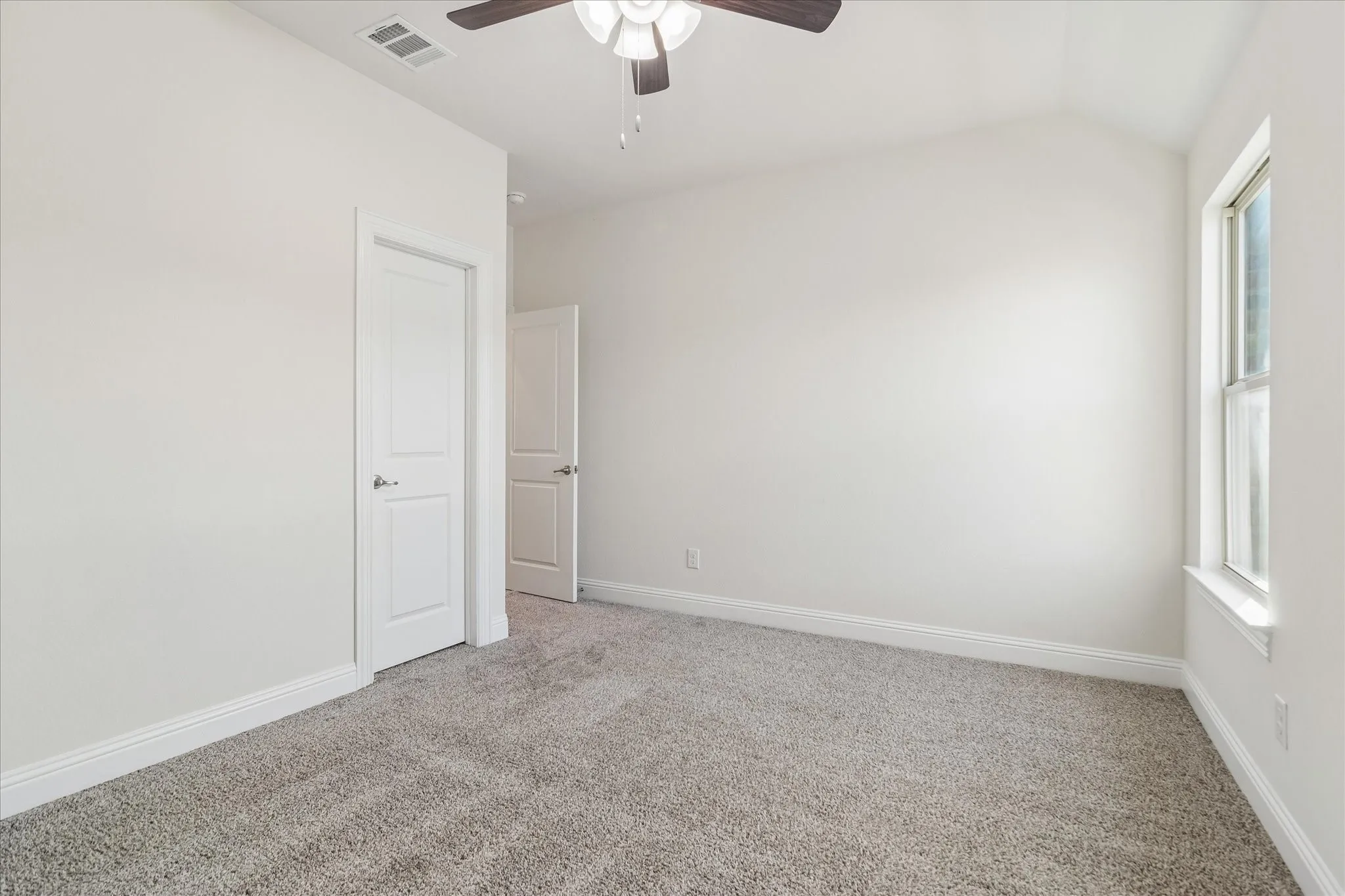 Carpeted flooring, vaulted ceiling, ceiling fan, white interior doors, and a window