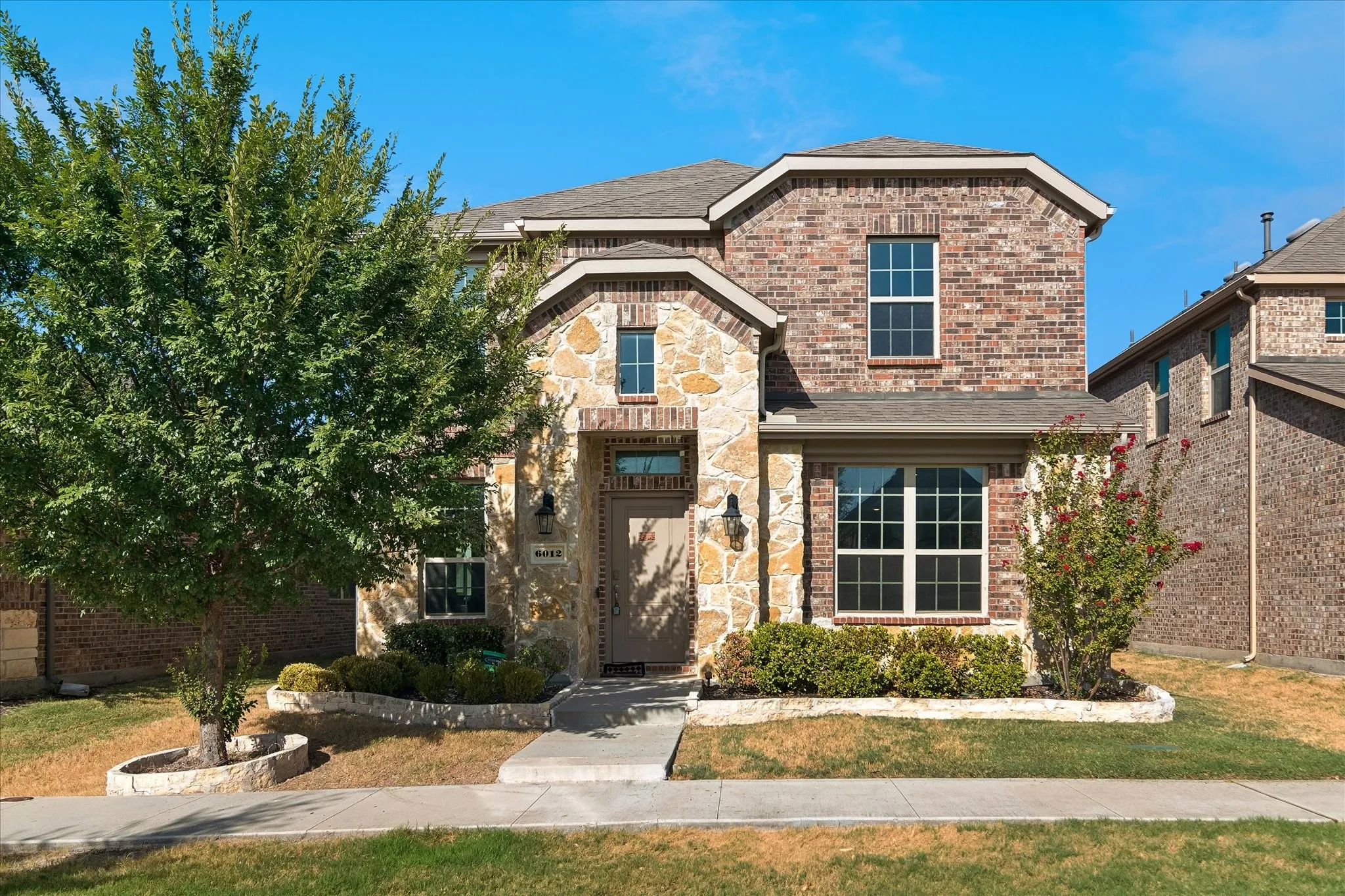Brick and stone facade with multiple window styles, established landscaping, and an inviting front entry