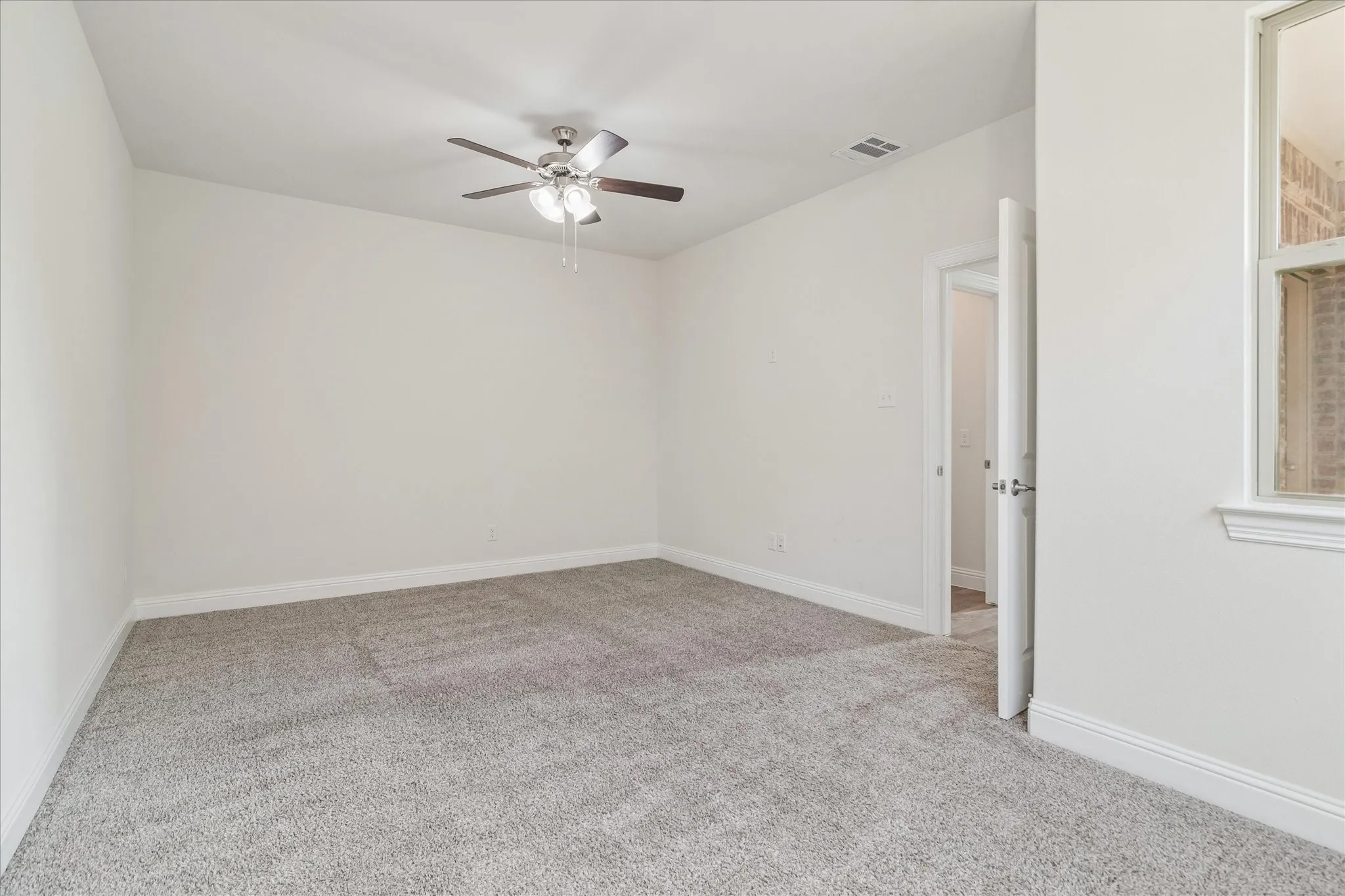 Spacious room featuring neutral carpeting, light-colored walls, a ceiling fan with integrated lighting, and a white-trimmed window