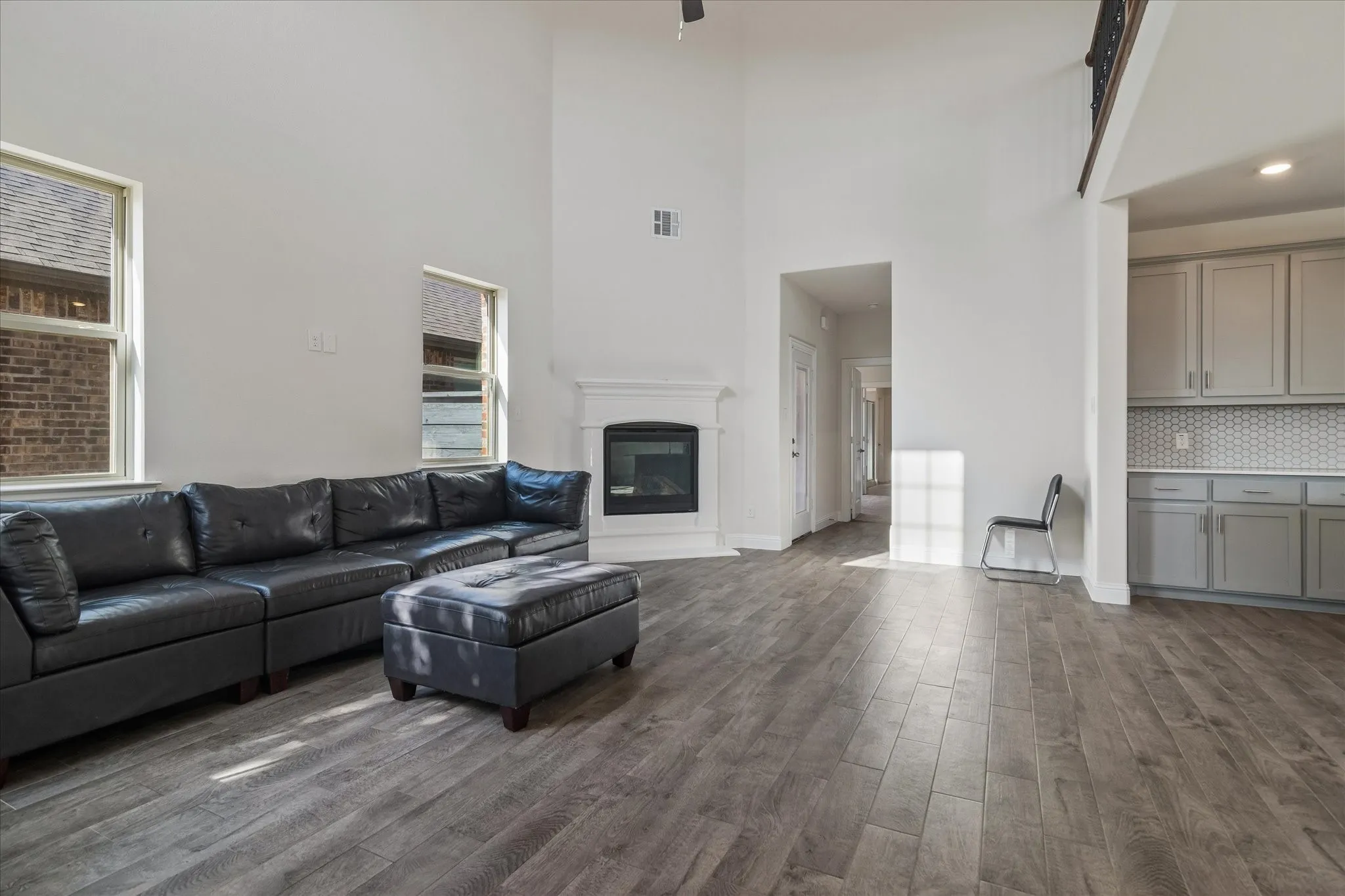 Two-story living area with wood-finish flooring, a white mantel fireplace, and high windows