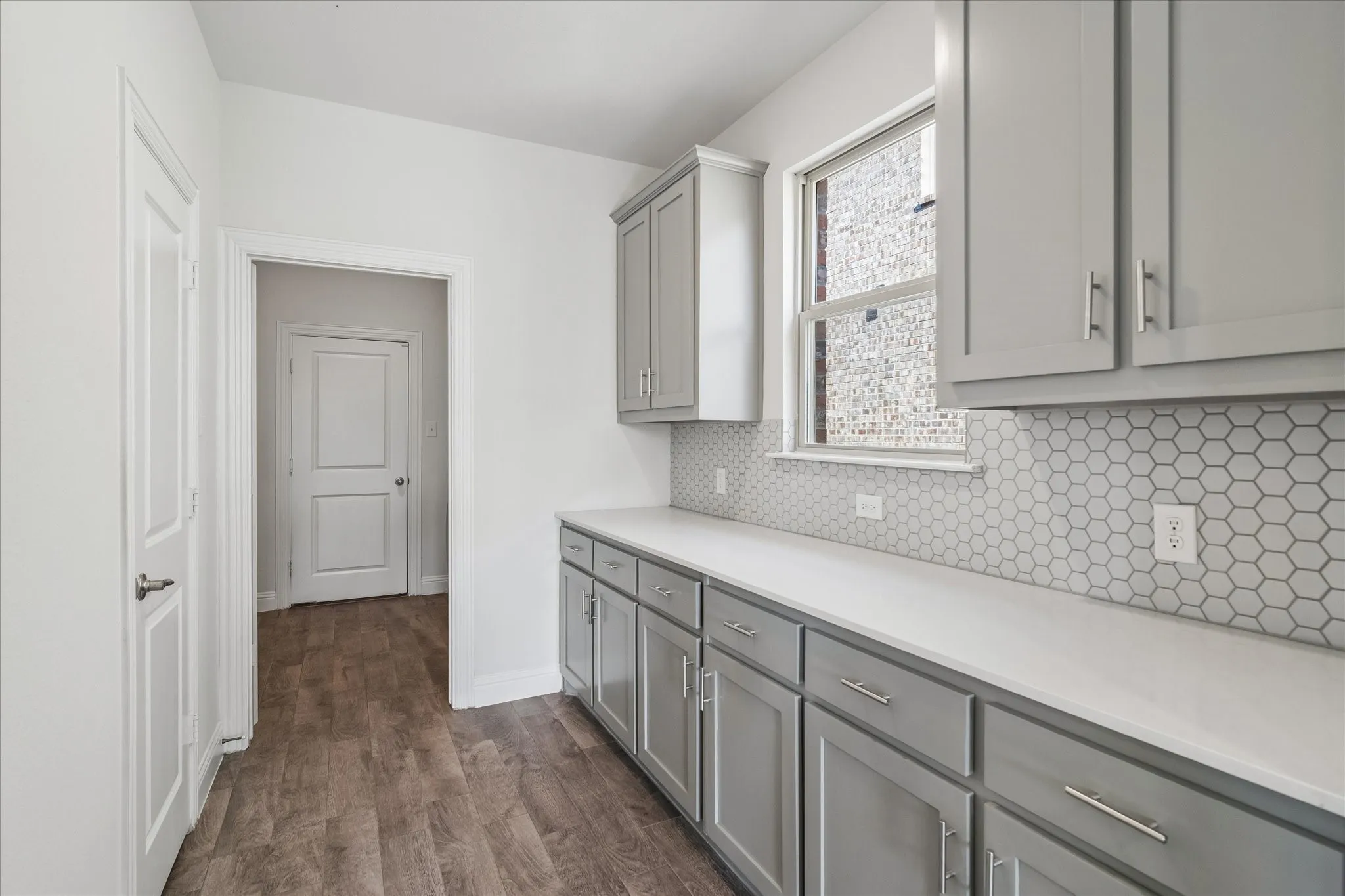 Gray shaker-style cabinetry with chrome hardware, white solid surface countertops, and hexagonal tile backsplash
